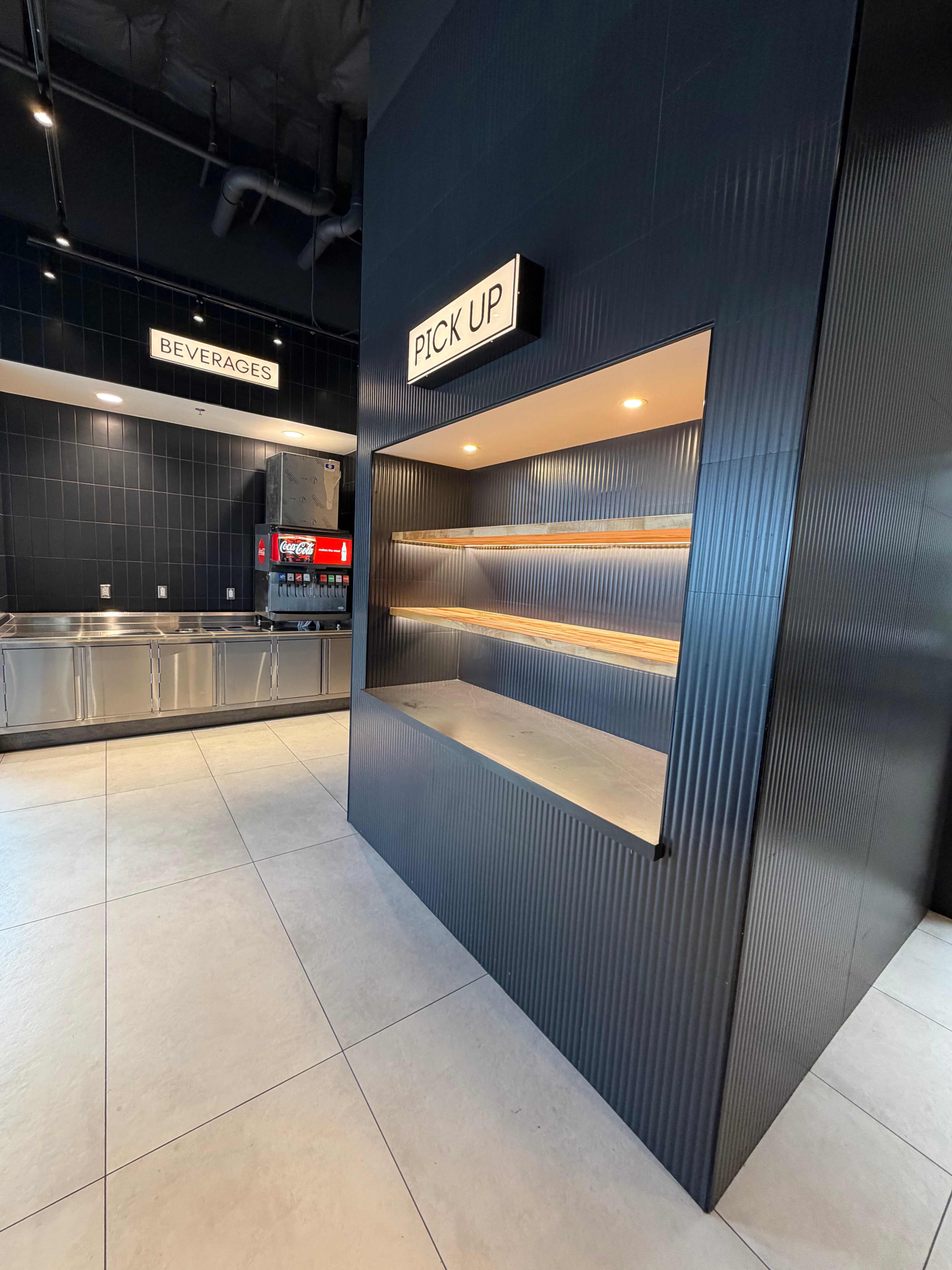 Restaurant pickup station with corrugated panel walls and illuminated shelving