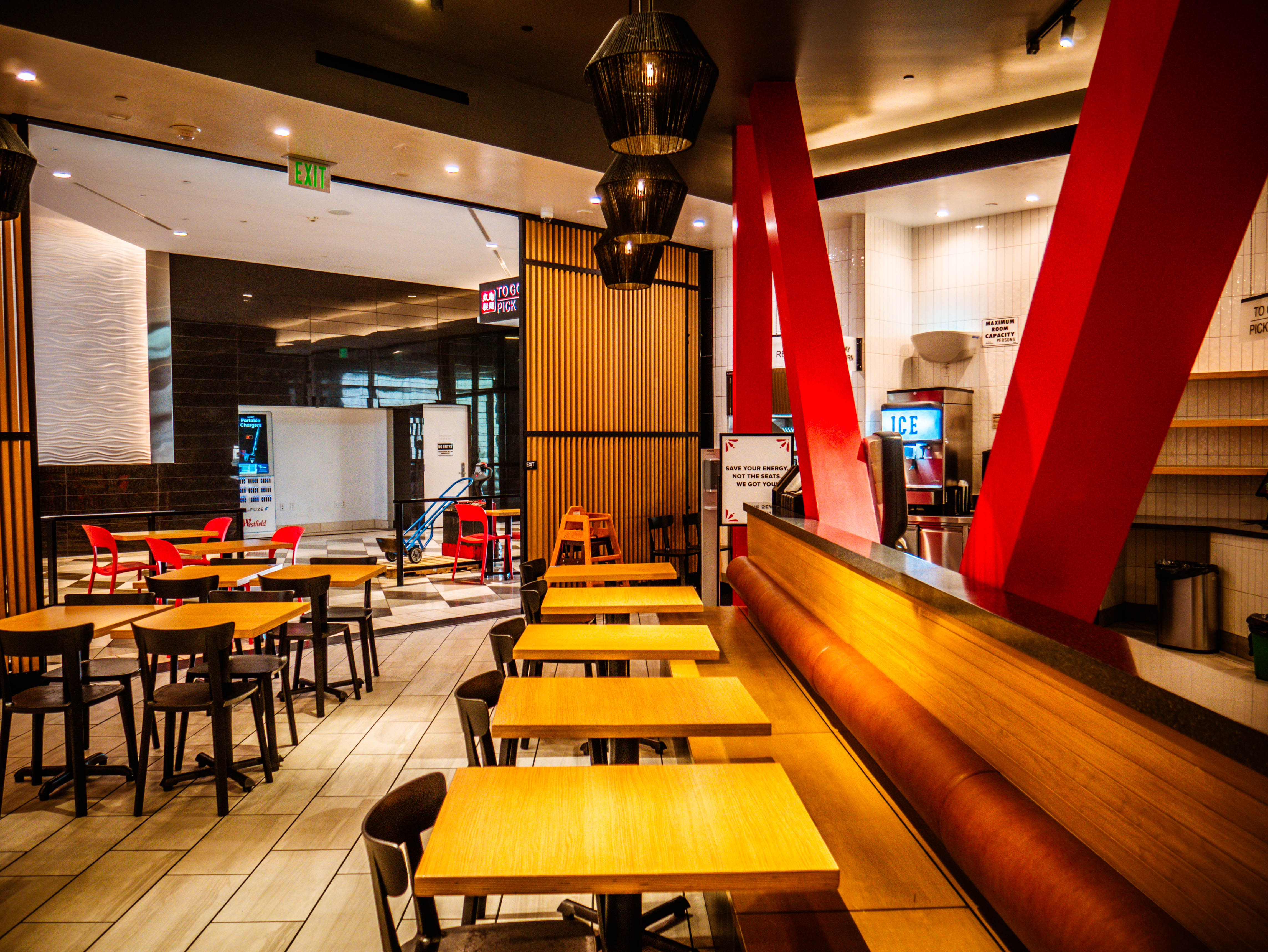 Comprehensive dining area with wooden banquette seating, red structural beams, pendant lighting, and seamless mall integration