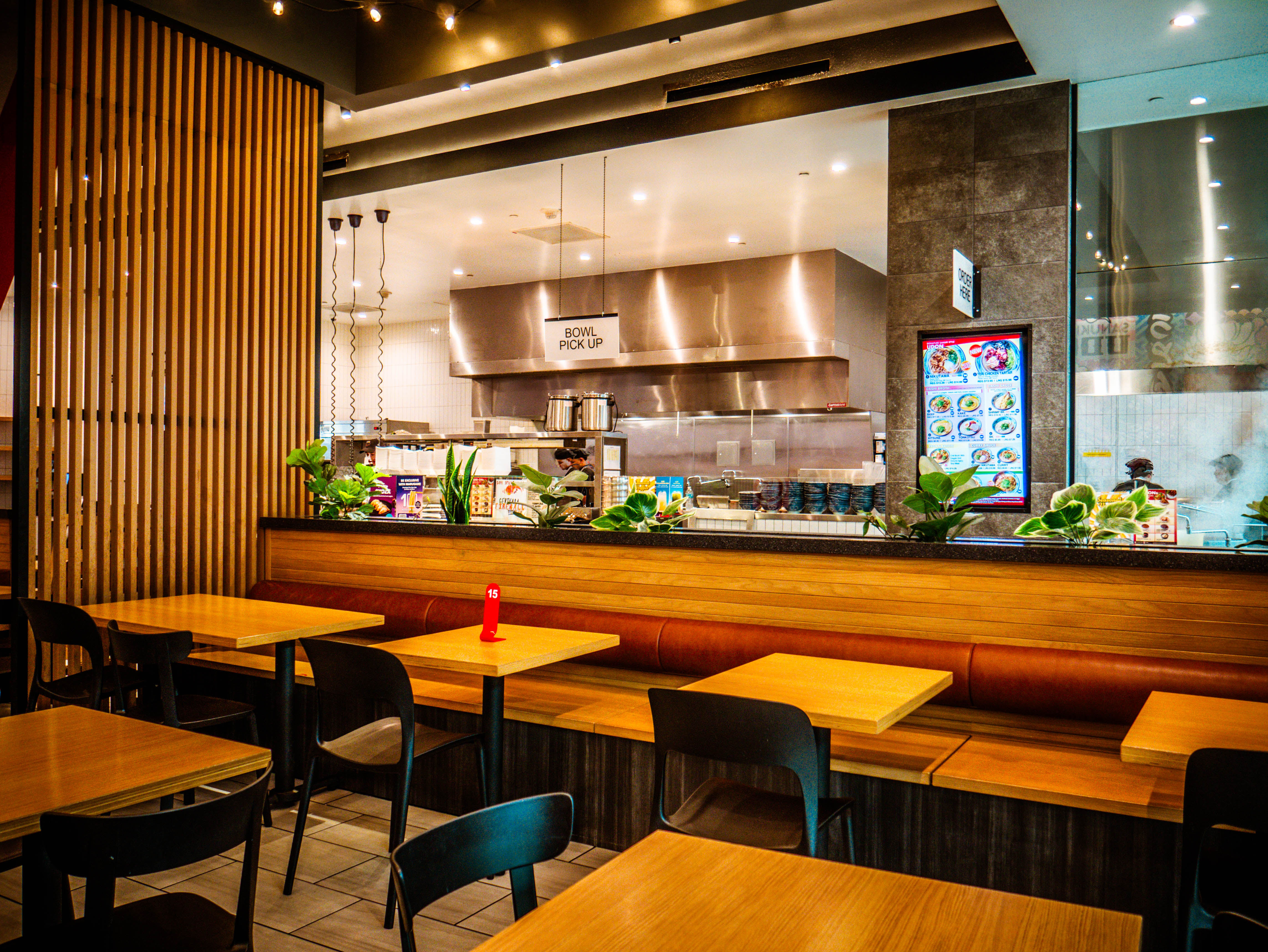 Counter seating area overlooking the open kitchen with wooden tables and view of professional cooking equipment