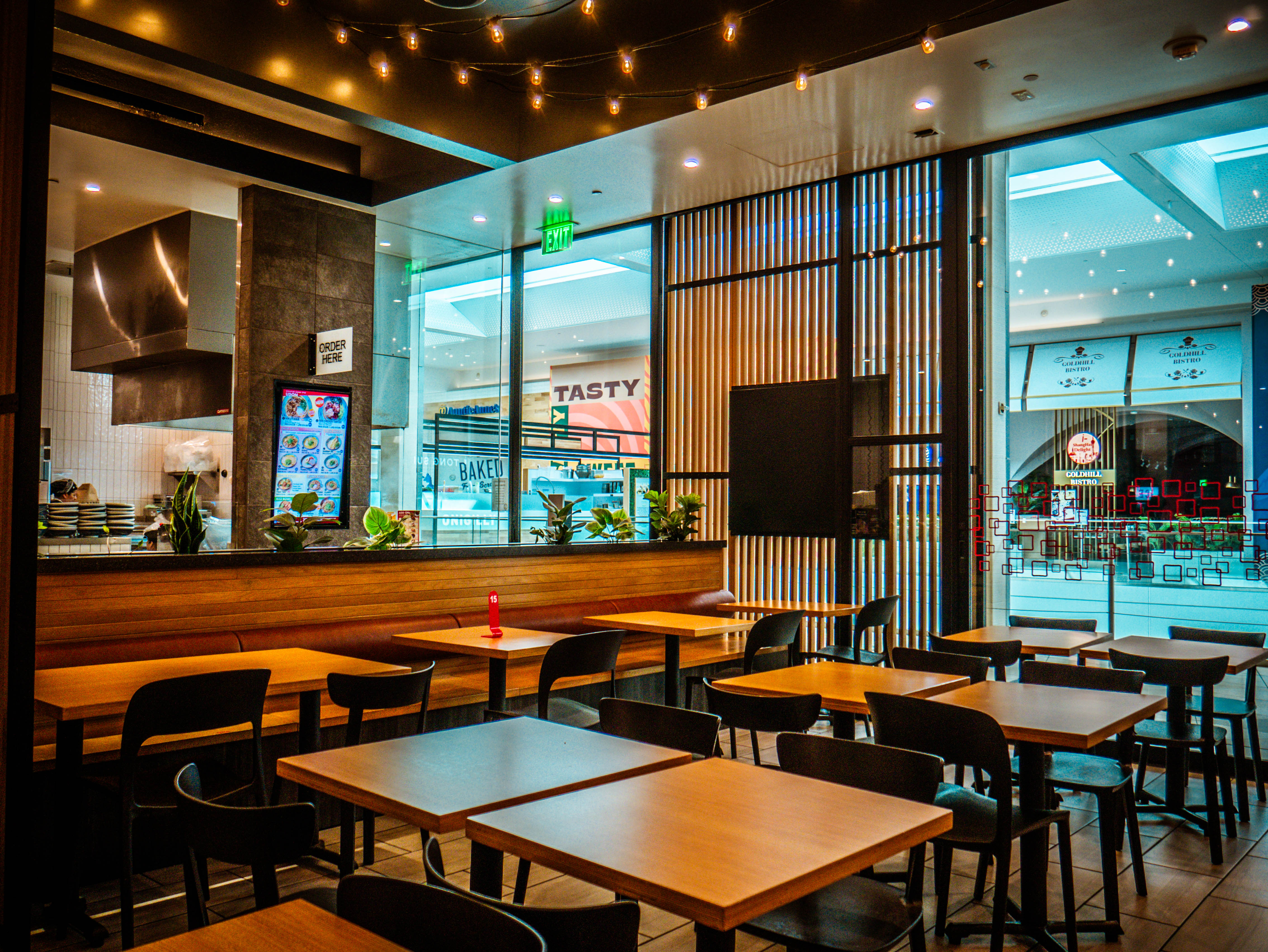 Seating area with view to Westfield Valley Fair mall corridor, featuring wooden banquettes and string lighting