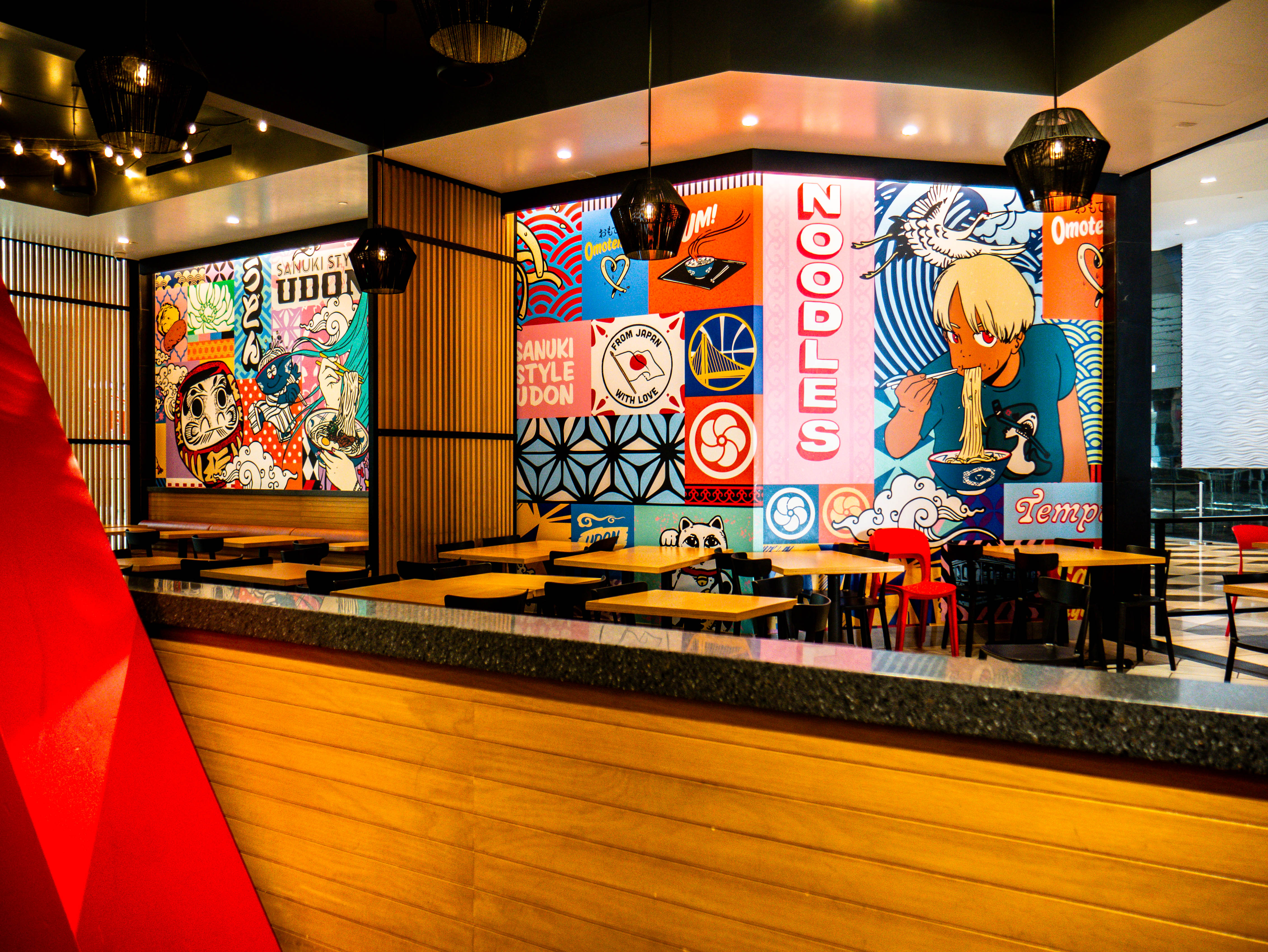 Elevated view of dining area showcasing vibrant murals, wooden tables, red structural elements, and comprehensive restaurant layout