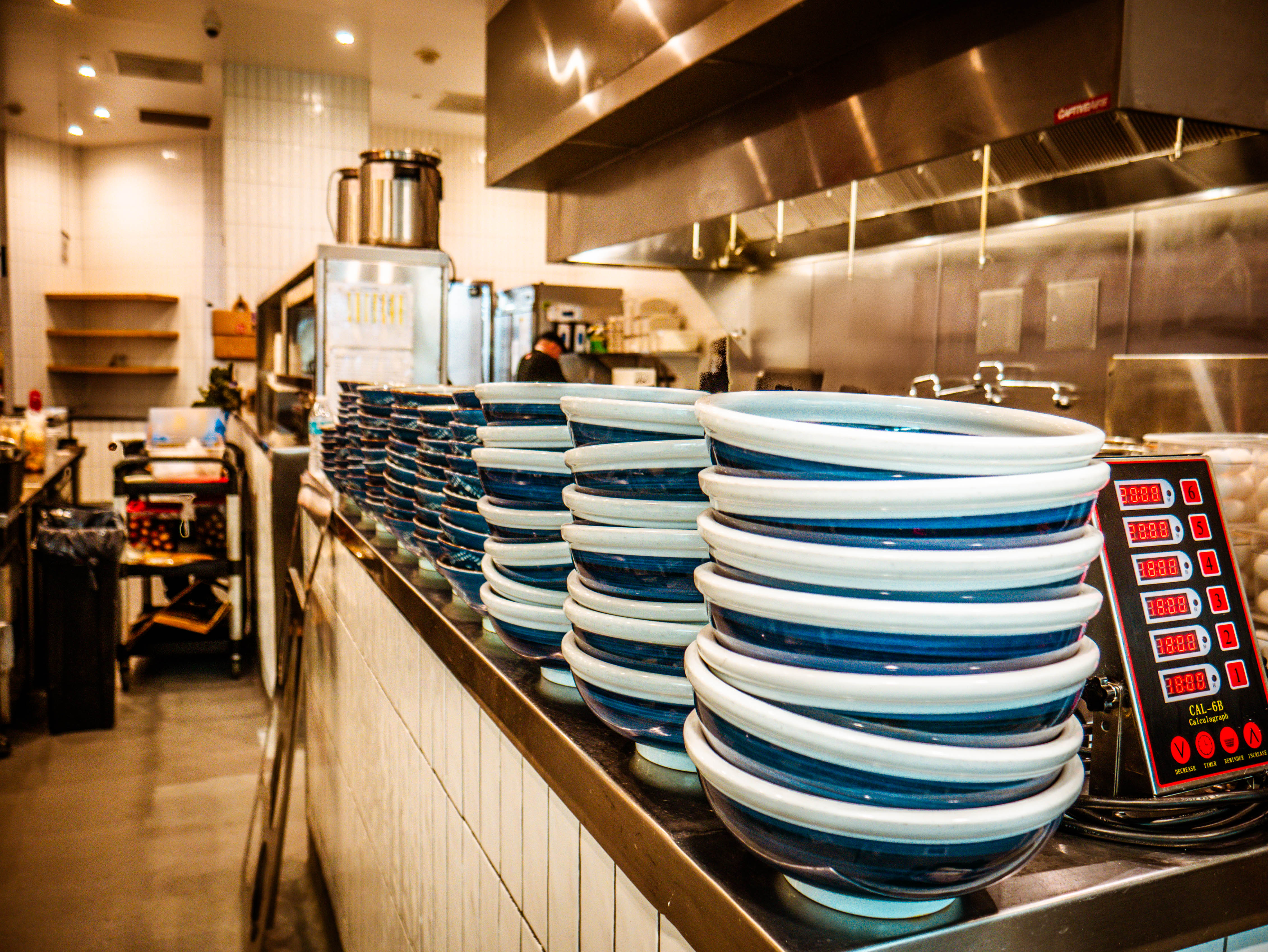 Professional kitchen organization with stacks of blue and white ceramic bowls, commercial equipment, and efficient storage systems