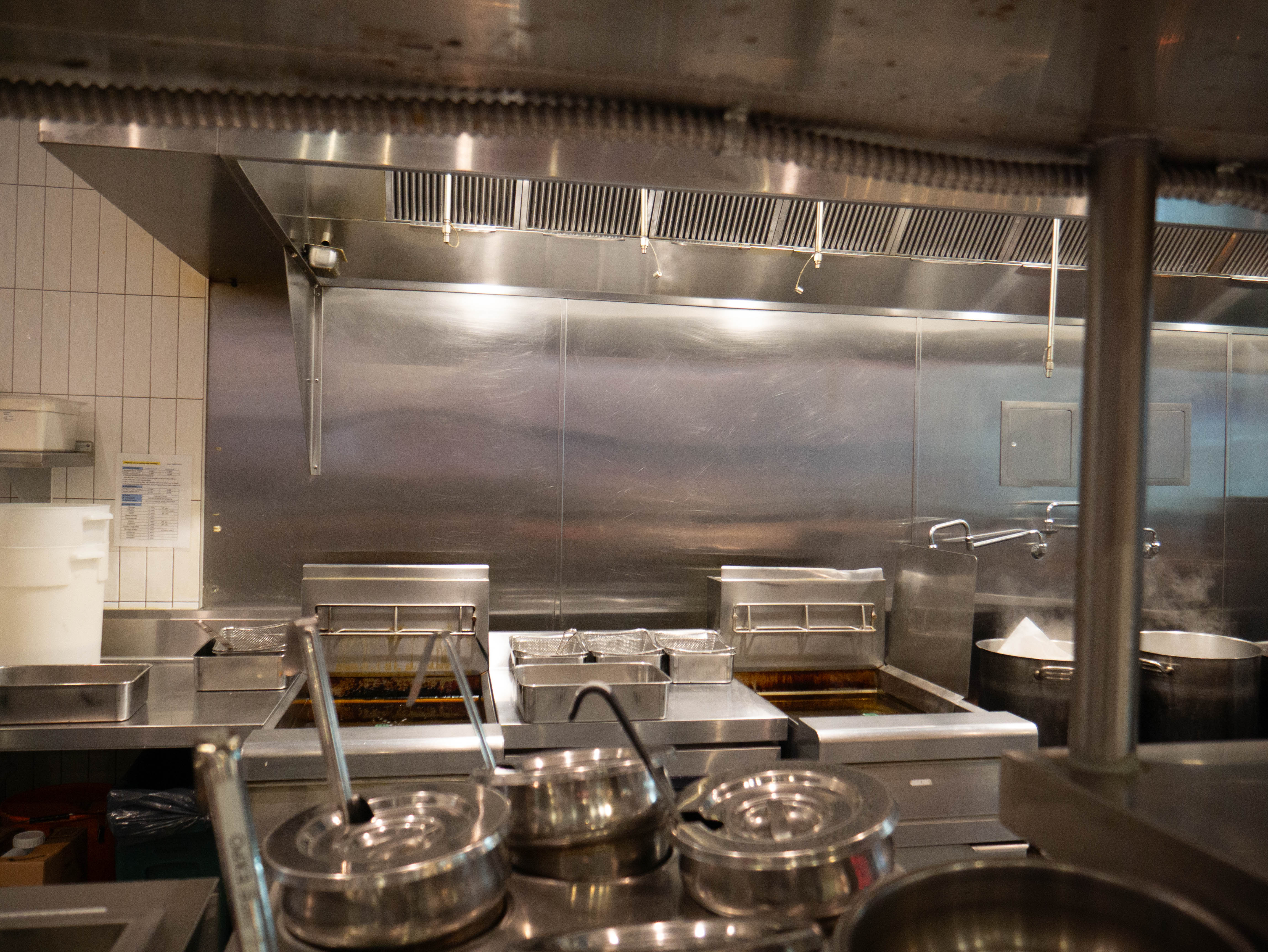 Clean professional kitchen service line with multiple cooking stations, advanced ventilation system, and stainless steel equipment