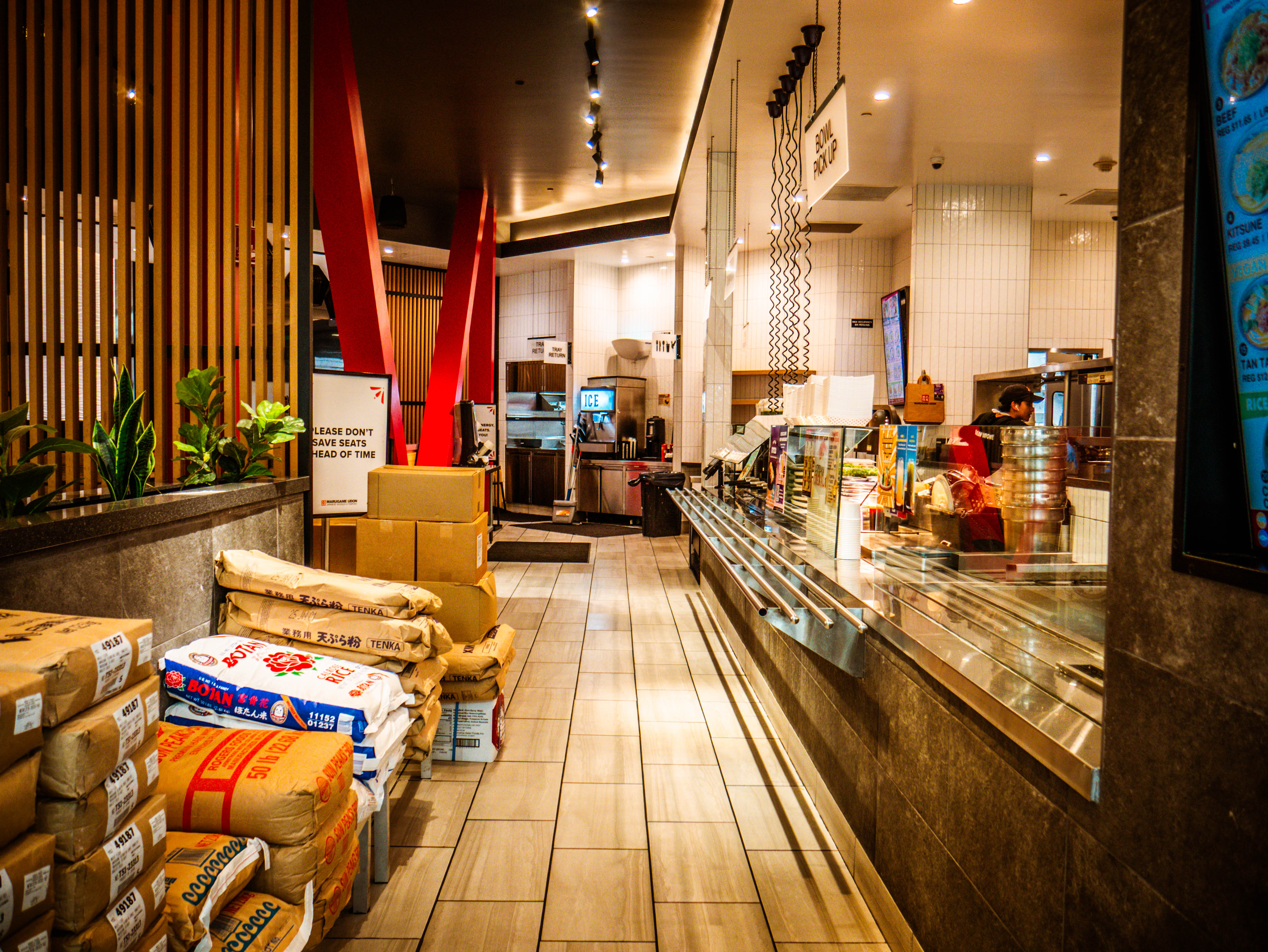 Professional kitchen service area with ingredient storage bags, red structural beams, and commercial equipment installation