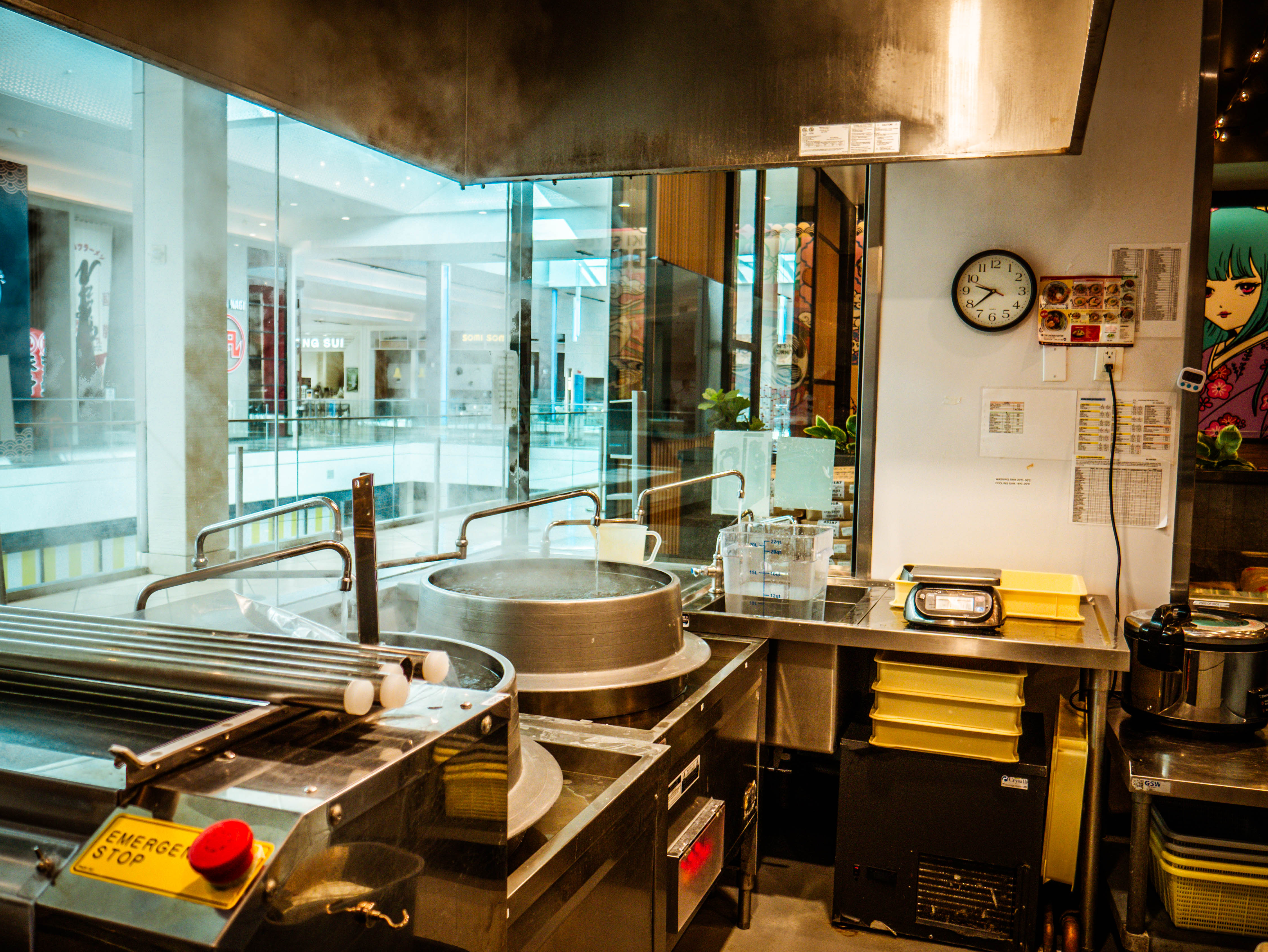 Kitchen workspace with copper udon cooking pot, mall view through windows, and professional equipment with emergency safety controls