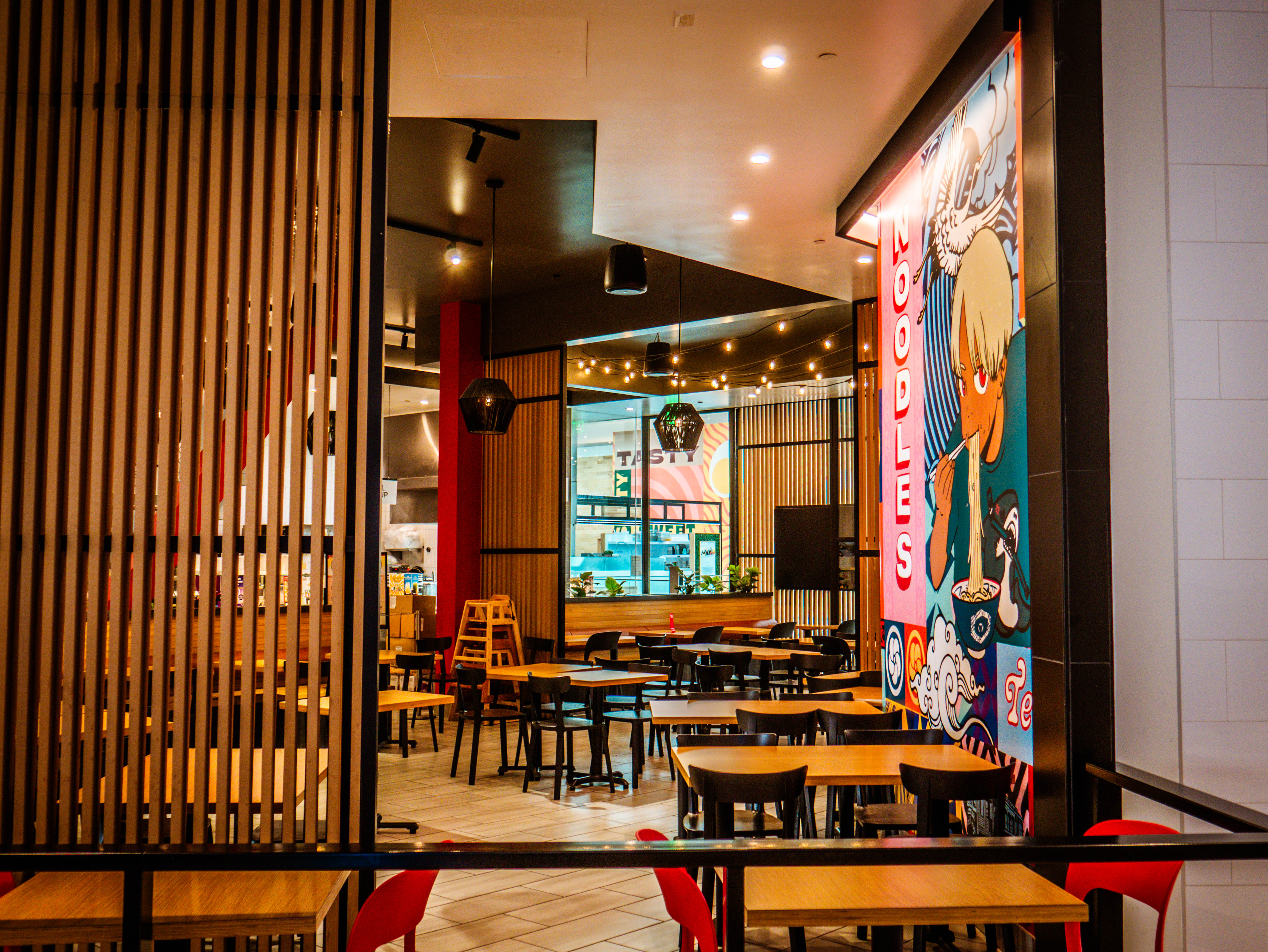 View from mall corridor into restaurant showing wooden slat privacy screens, dining areas, and sophisticated integration design