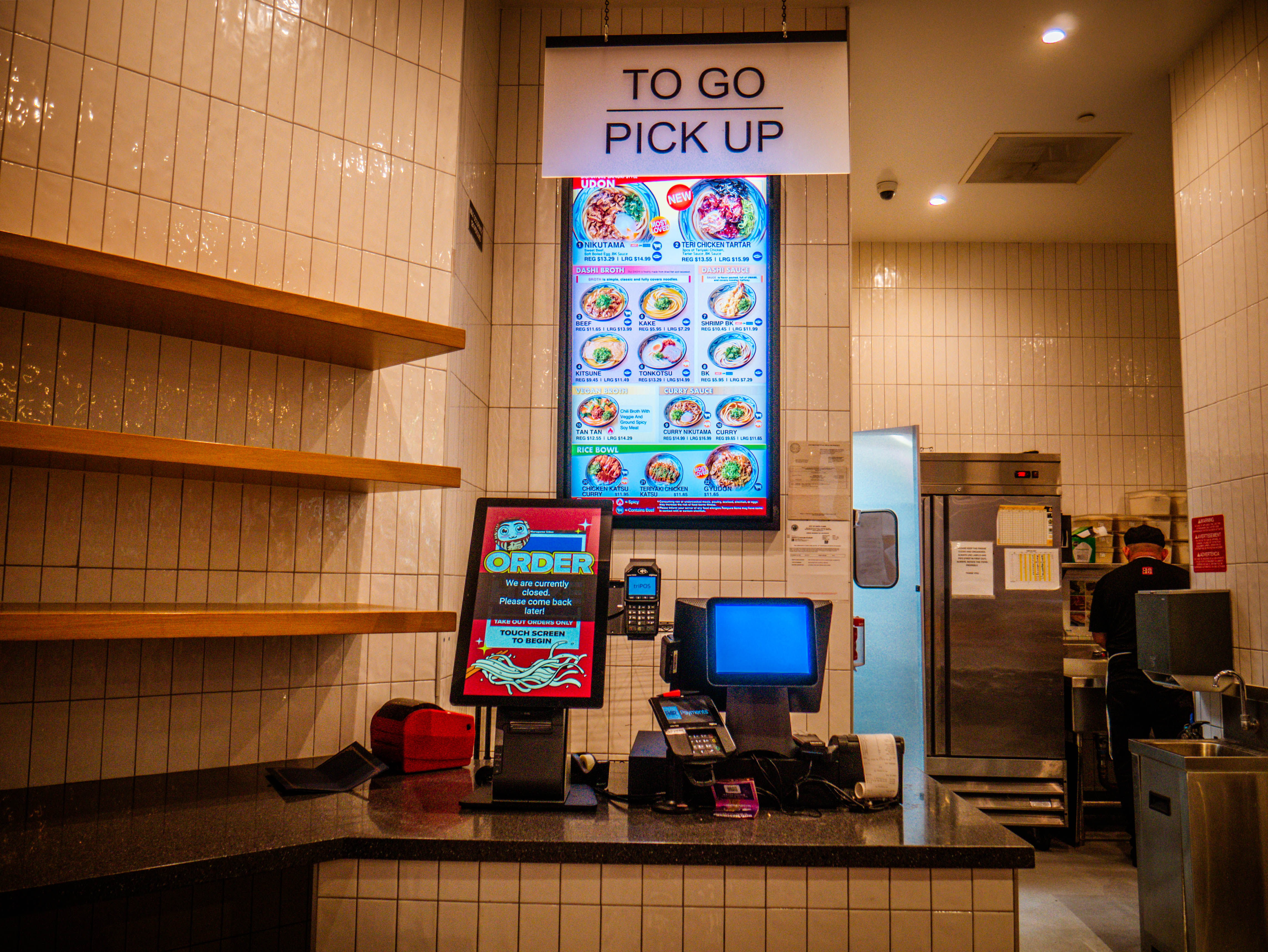 To-go pickup counter featuring digital menu displays, POS systems, and self-service ordering kiosks