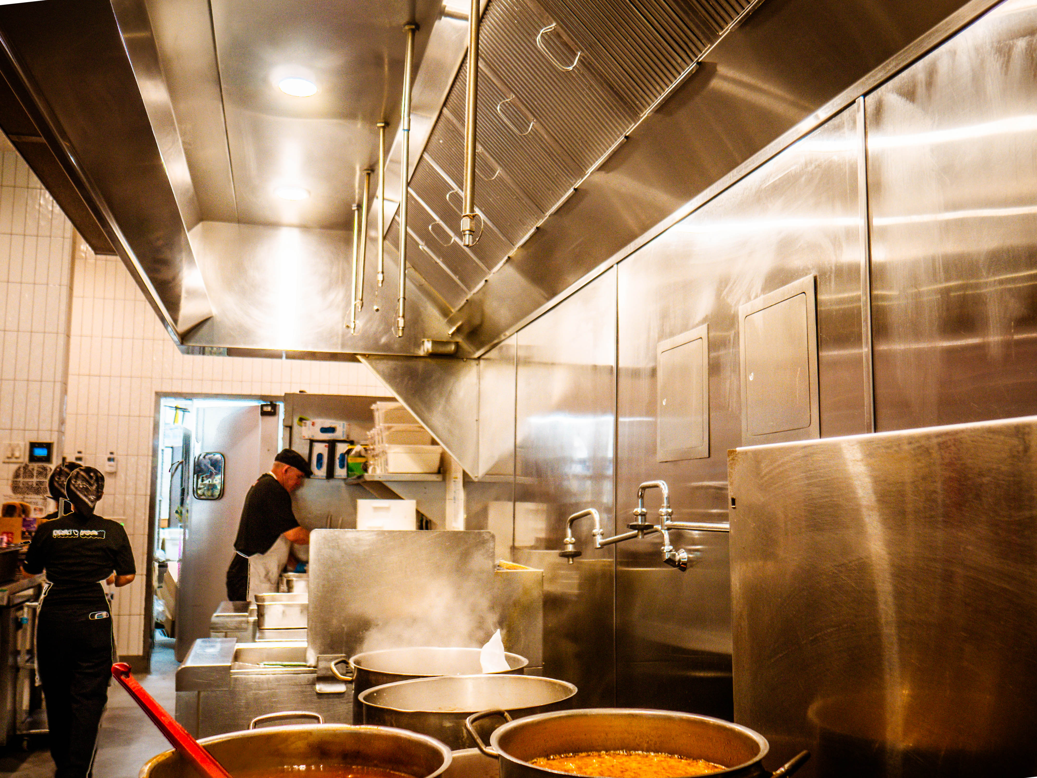 Professional kitchen in full operation with chefs working, stainless steel equipment, ventilation hood, and active cooking process