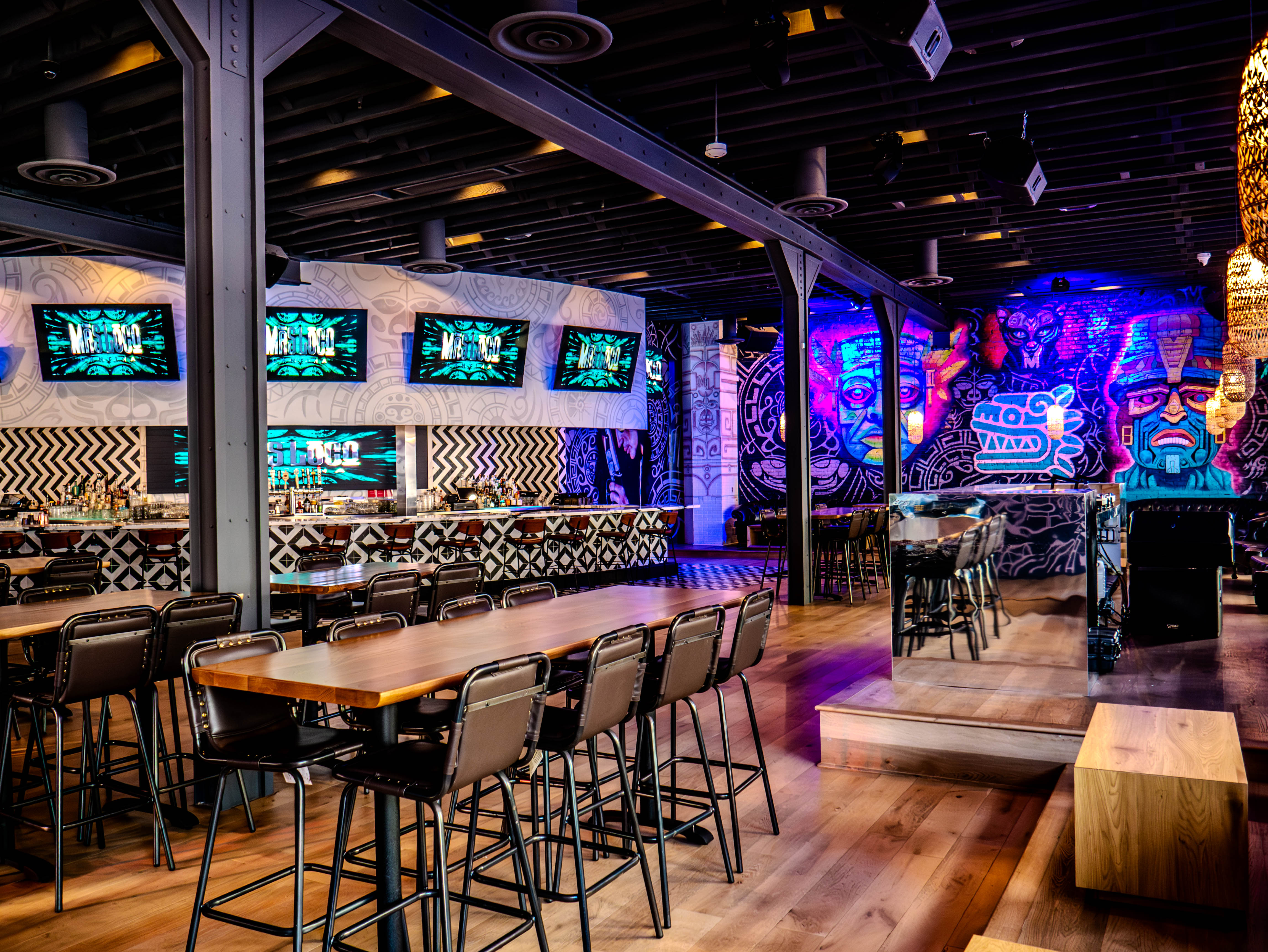 Comprehensive view of bar and dining areas with geometric patterns and industrial ceiling