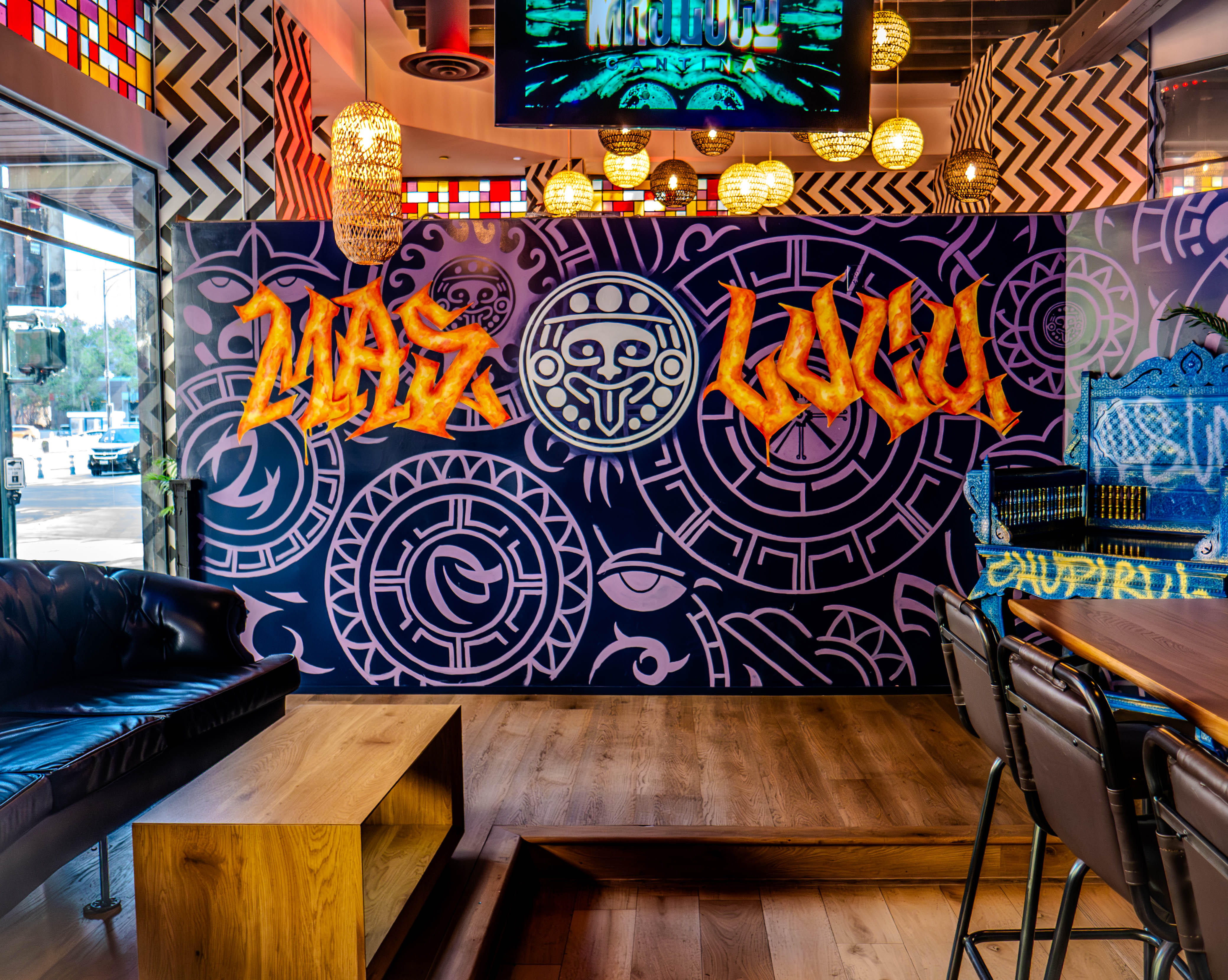 Dining area featuring prominent Mas Loco signage with purple Aztec murals and leather seating