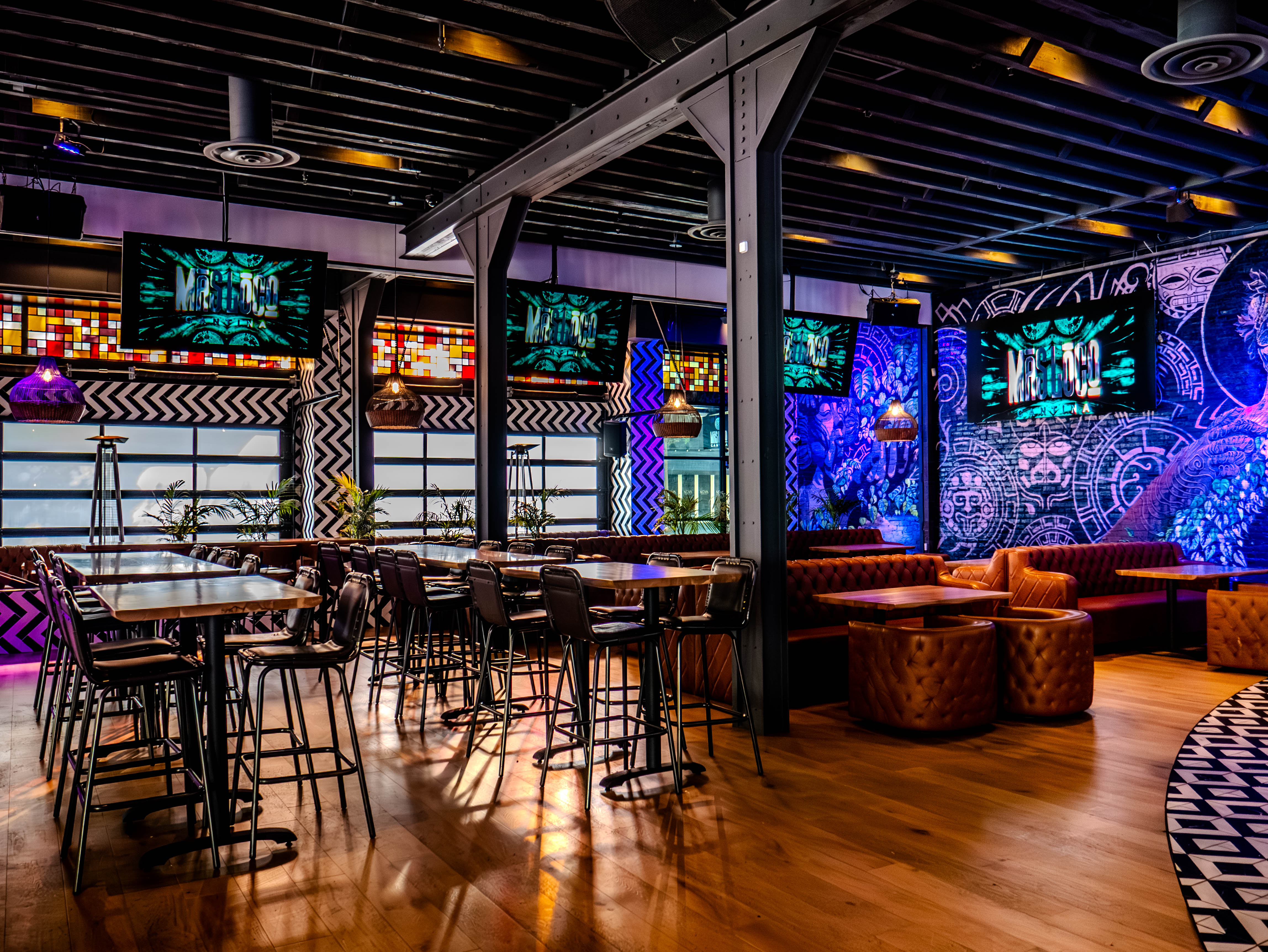 High-top dining area with vibrant Aztec murals and industrial ceiling