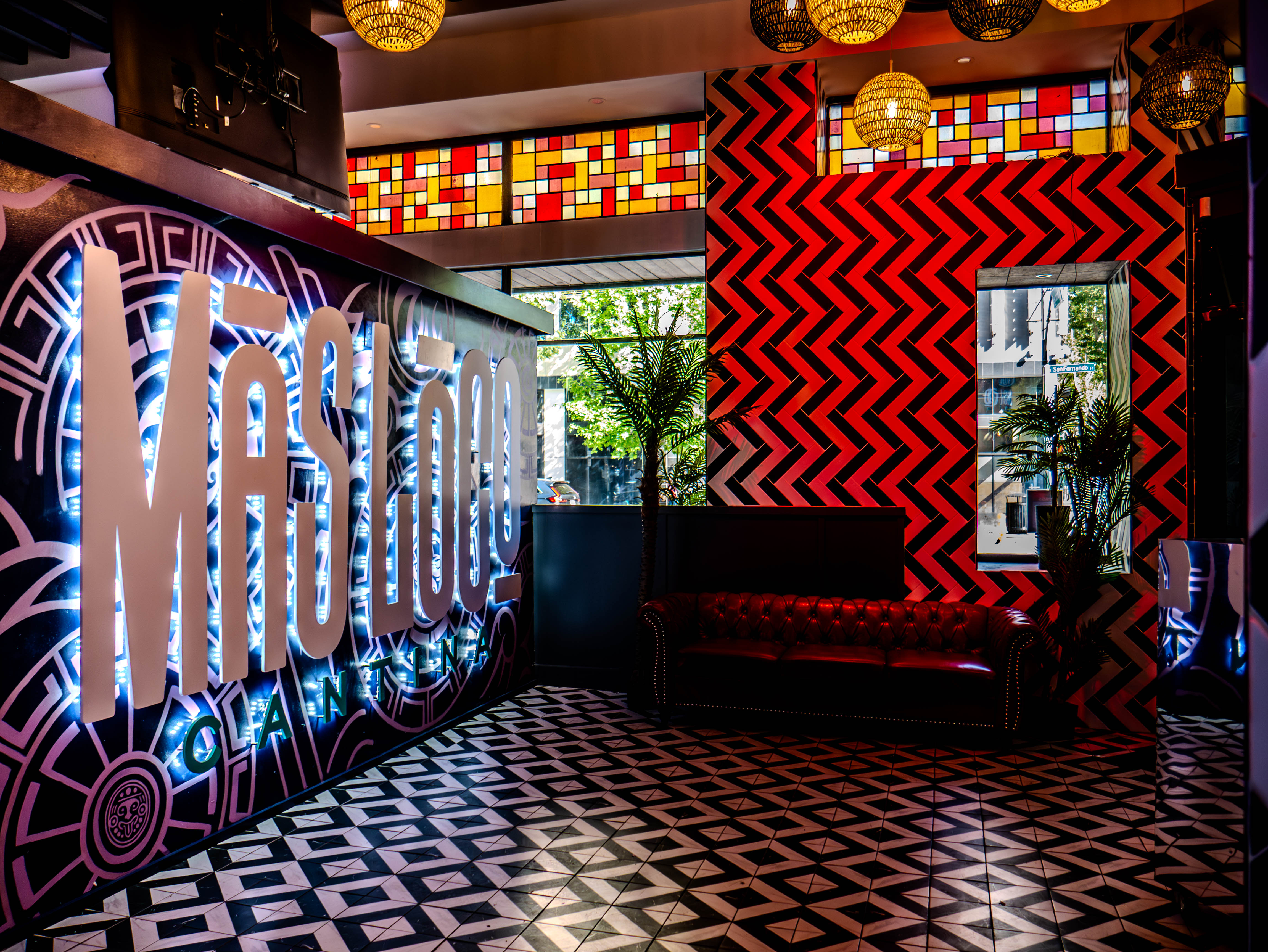 Restaurant entrance featuring large Mas Loco signage with geometric patterns and colorful stained glass
