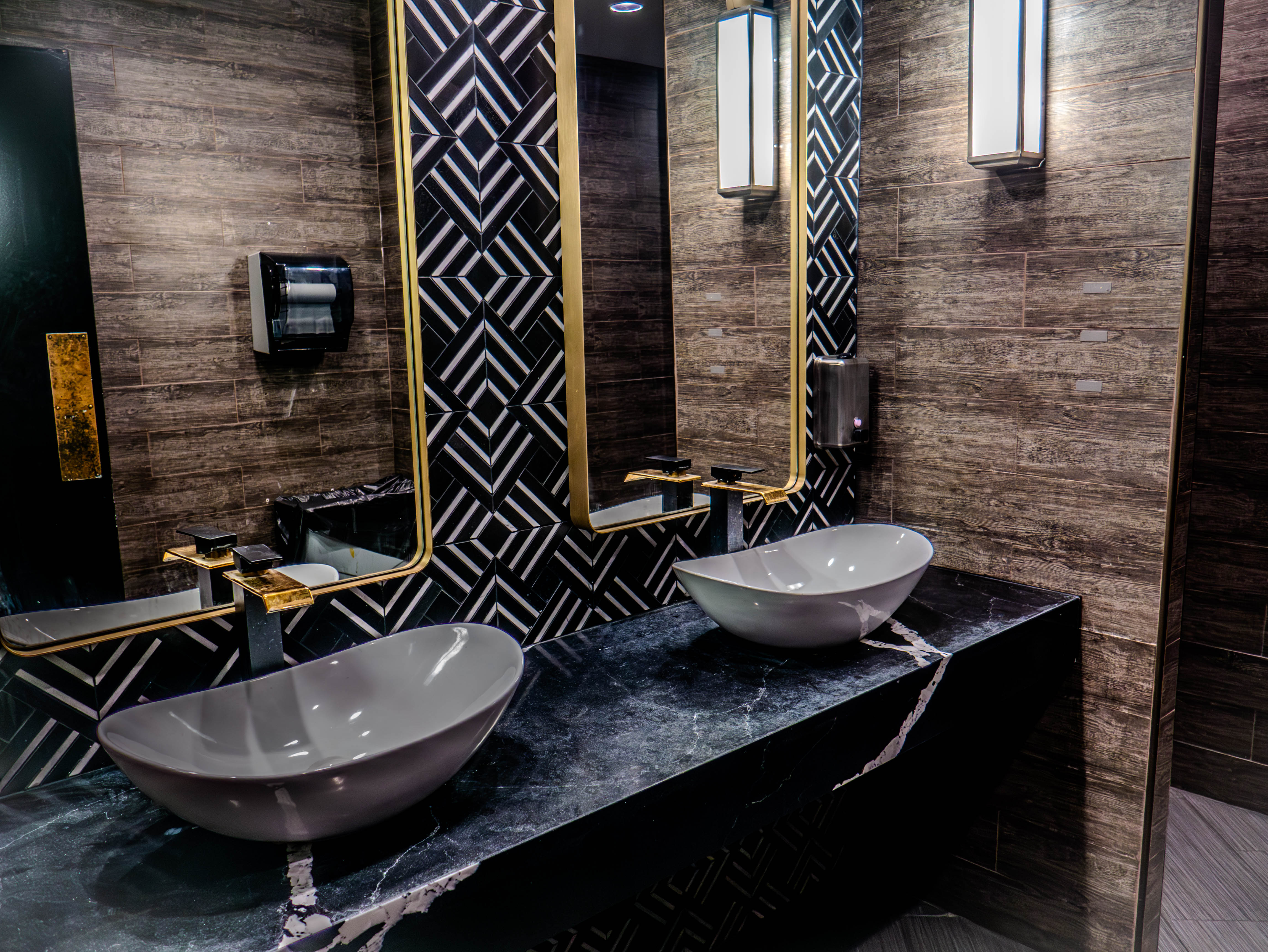 Luxury restroom with vessel sinks, black marble countertops, and geometric tile patterns