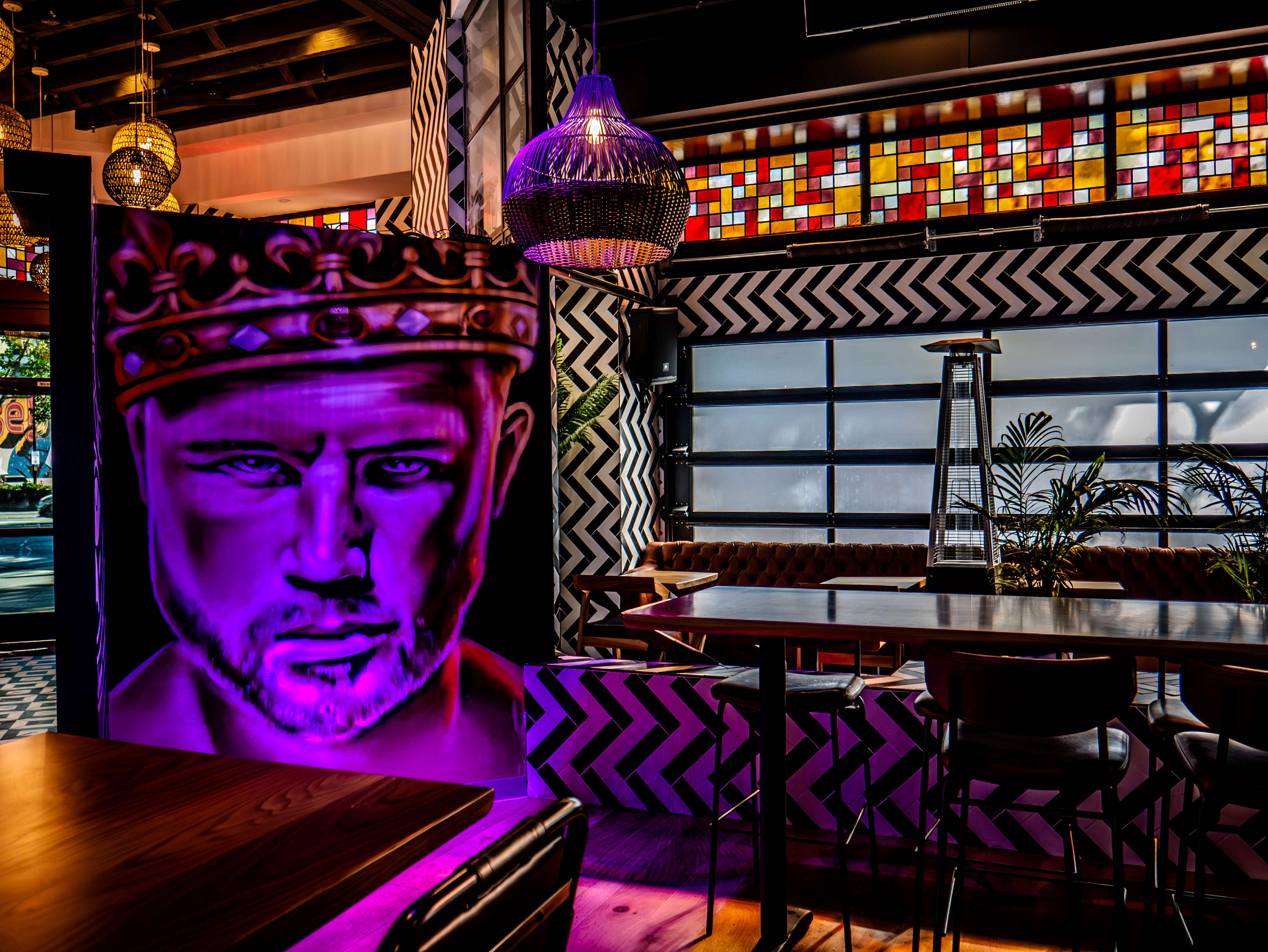 Dramatic purple mural of boxer Canelo Alvarez with Aztec crown and high-top seating with colorful stained glass