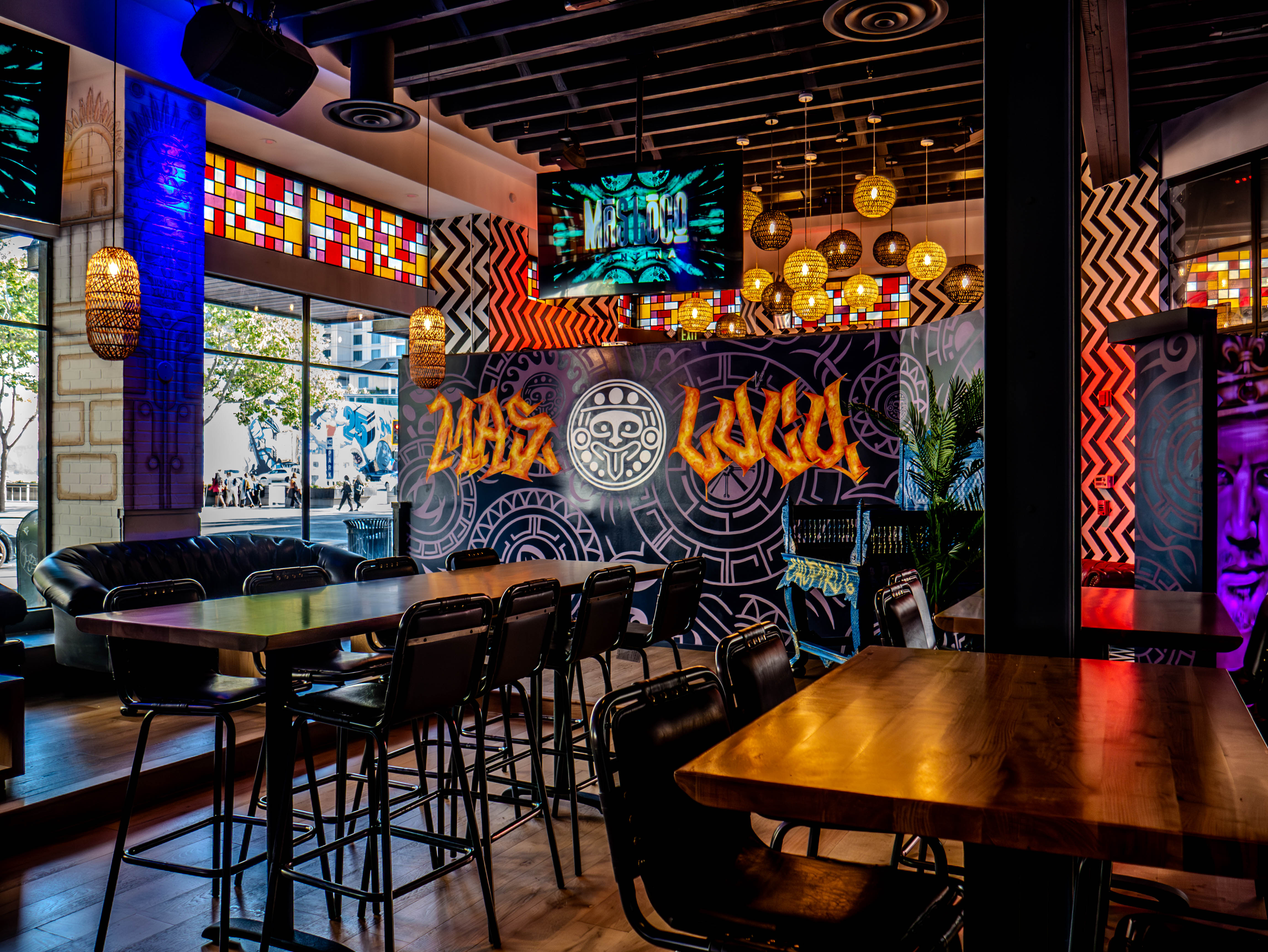High-top dining area showcasing the custom Mas Loco signage and colorful stained glass ceiling