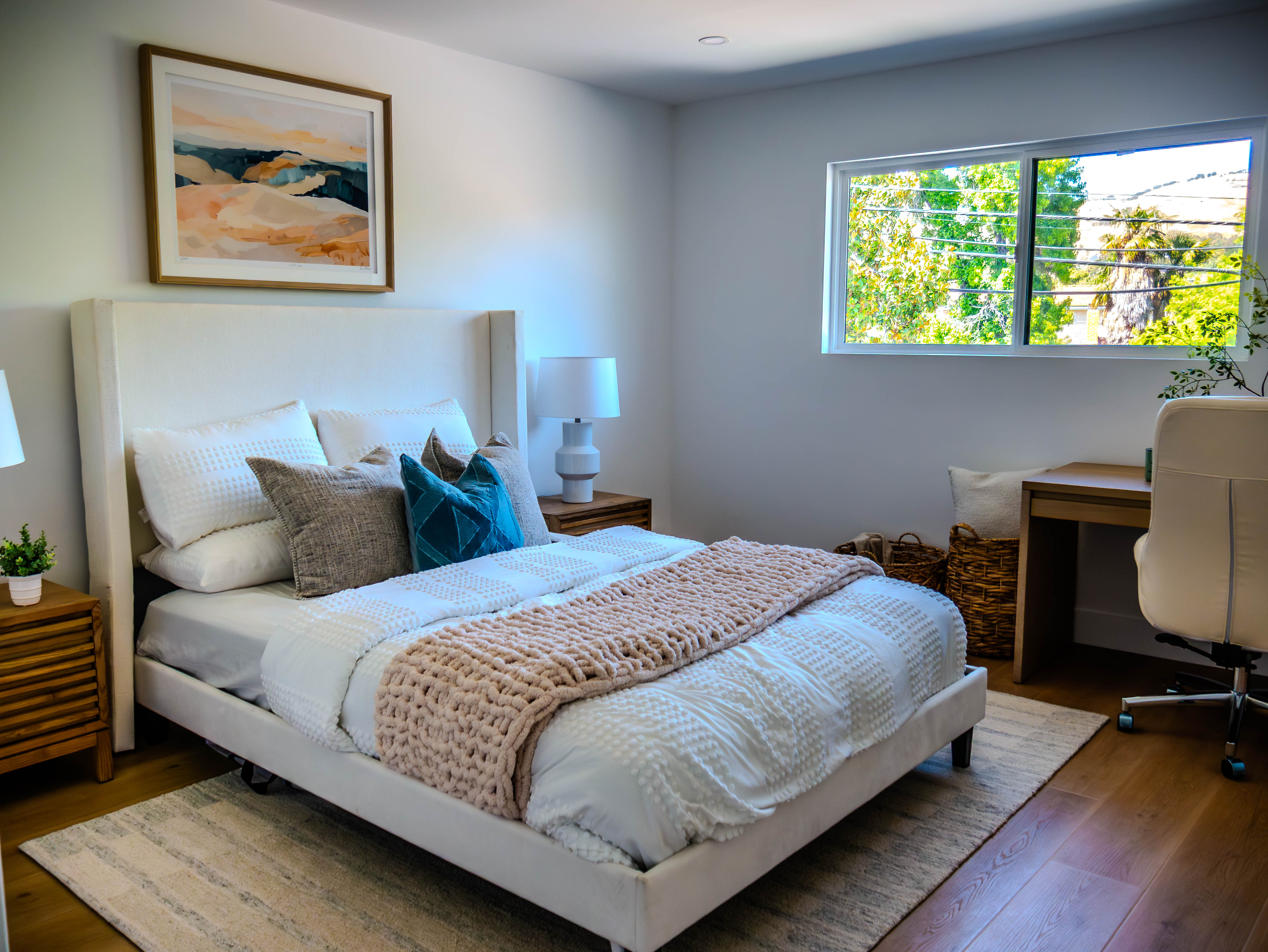 Versatile bedroom with integrated office area, white upholstered bed, contemporary artwork, and workspace with modern desk and chair