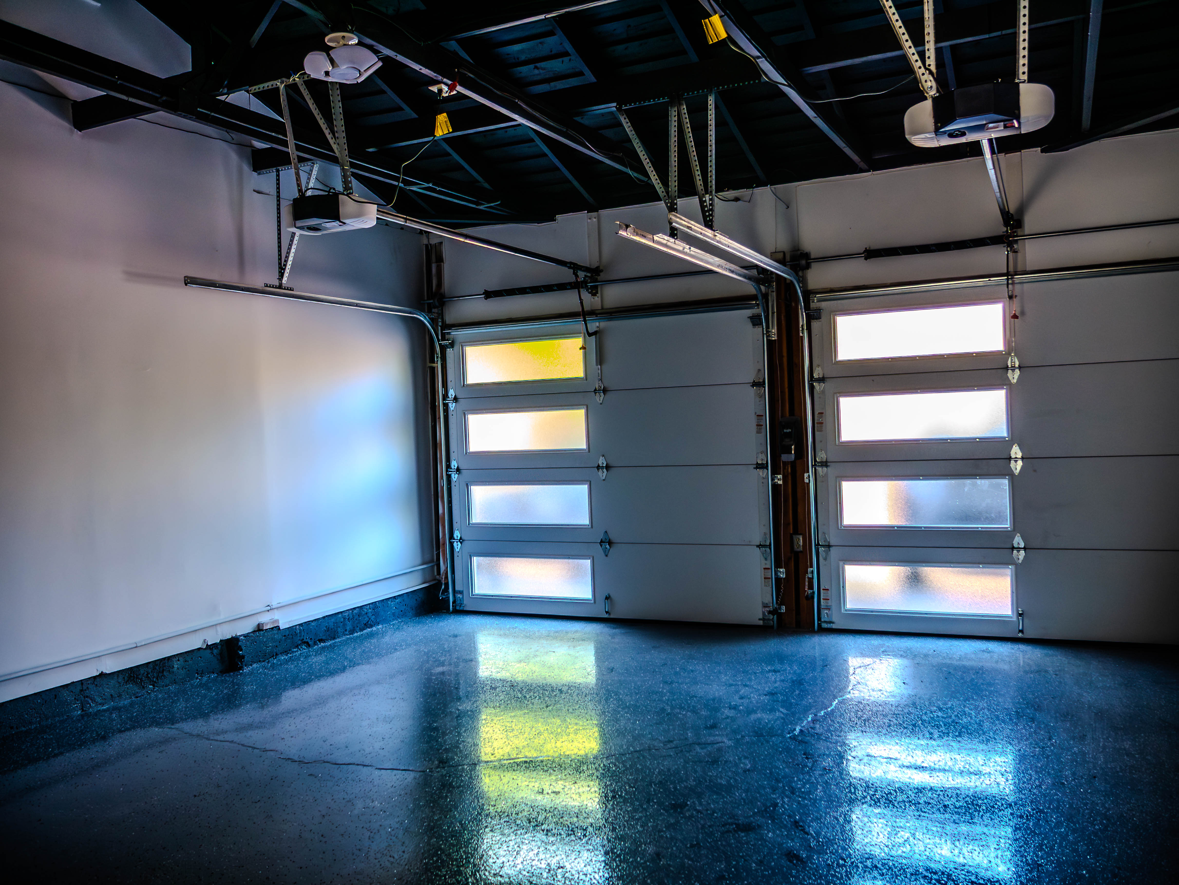 Modern garage interior with stunning polished blue concrete floors, overhead doors with windows, and professional lighting