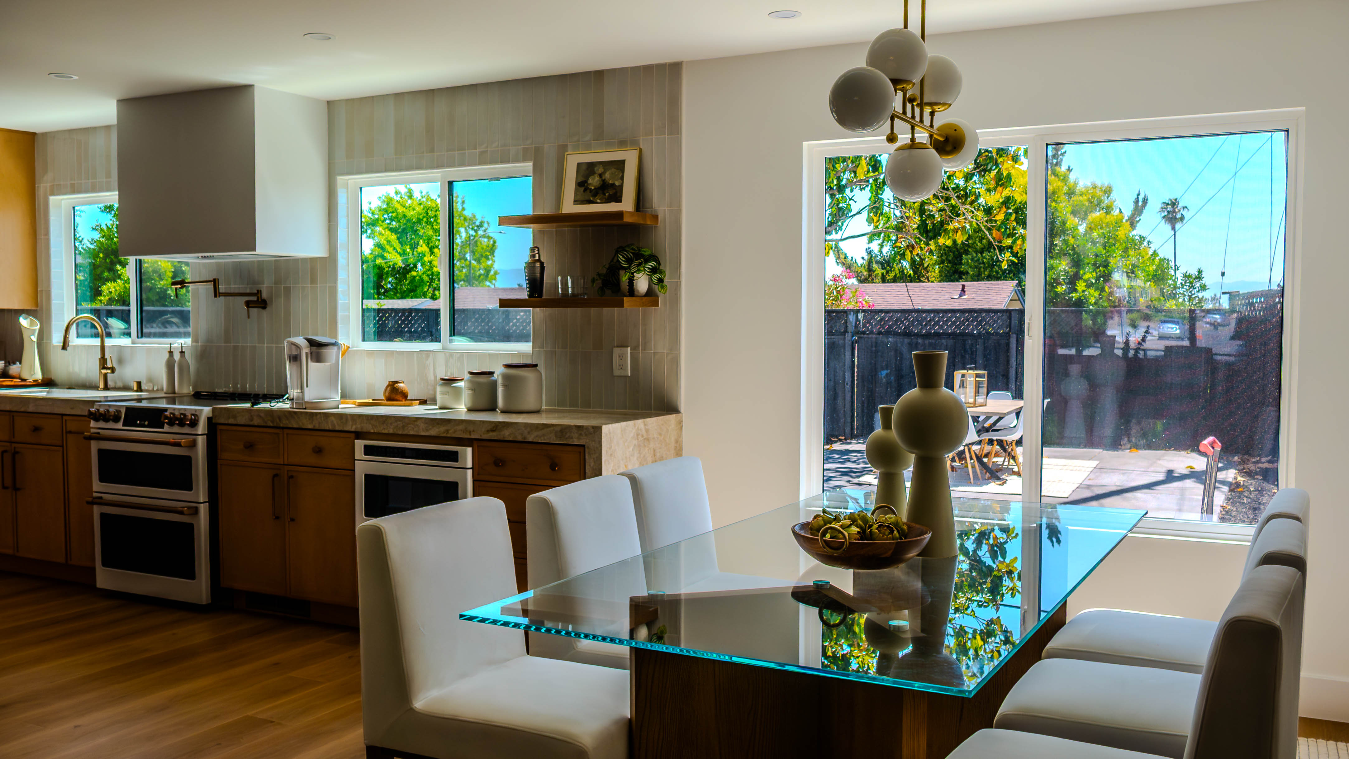 Modern kitchen with wooden cabinetry, vertical tile backsplash, high-end appliances, and glass dining table