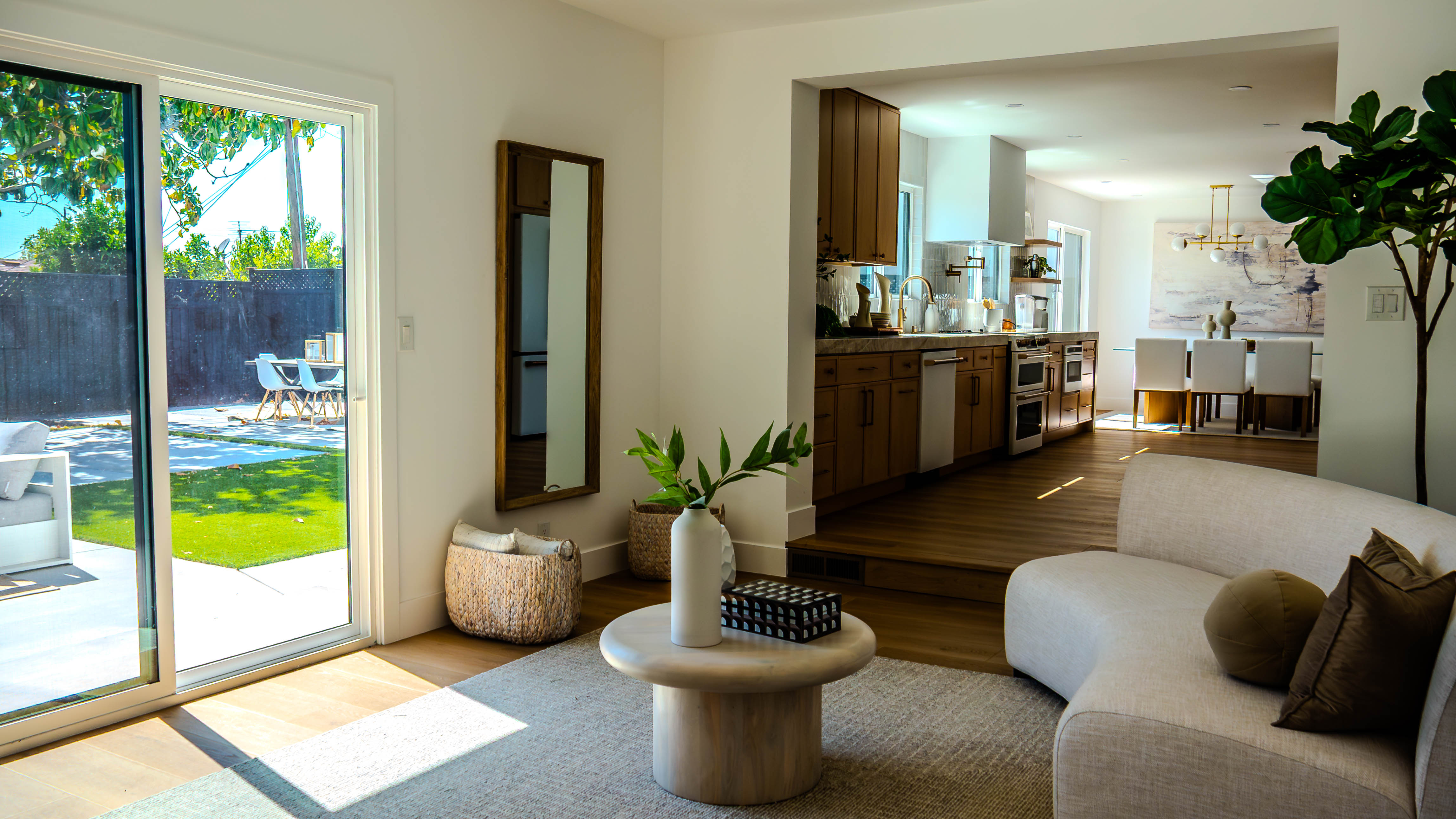 Living room with large sliding glass doors opening to backyard, neutral furniture, and kitchen in background