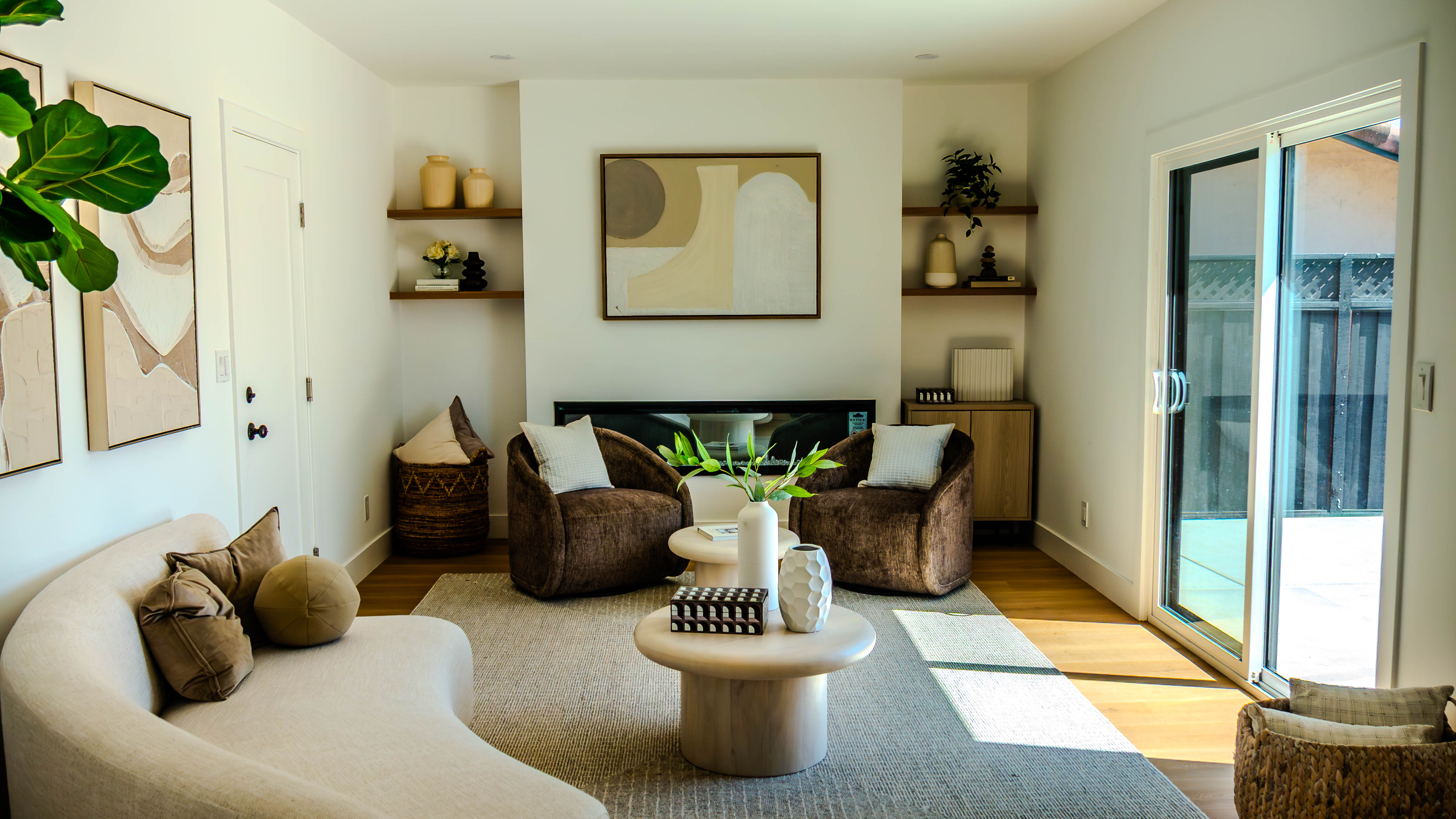 Beautifully designed living room with curved white sofa, brown accent chairs, built-in shelving around fireplace, and contemporary artwork
