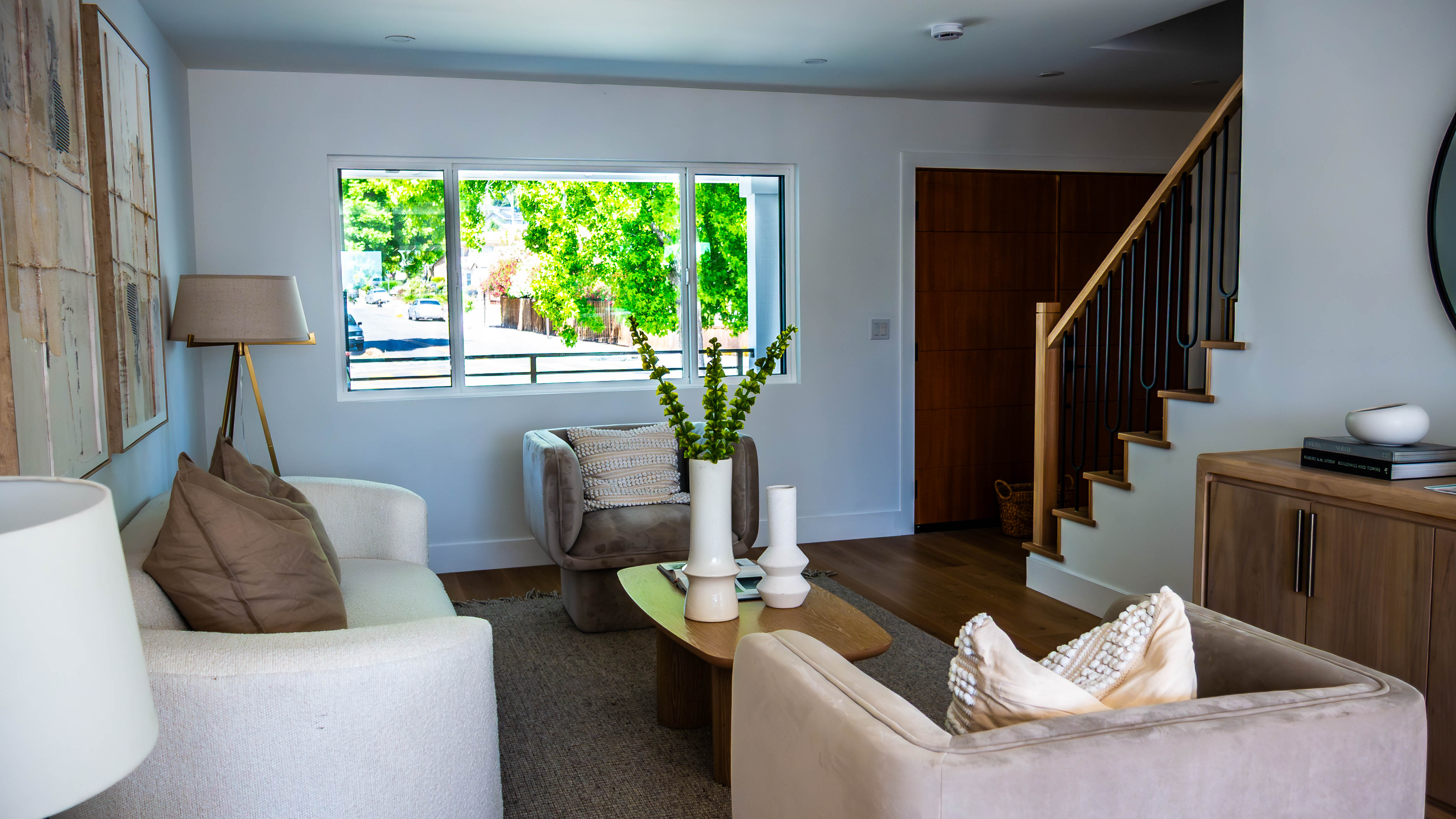 Contemporary living room with neutral furniture, modern staircase, large windows, and minimalist design