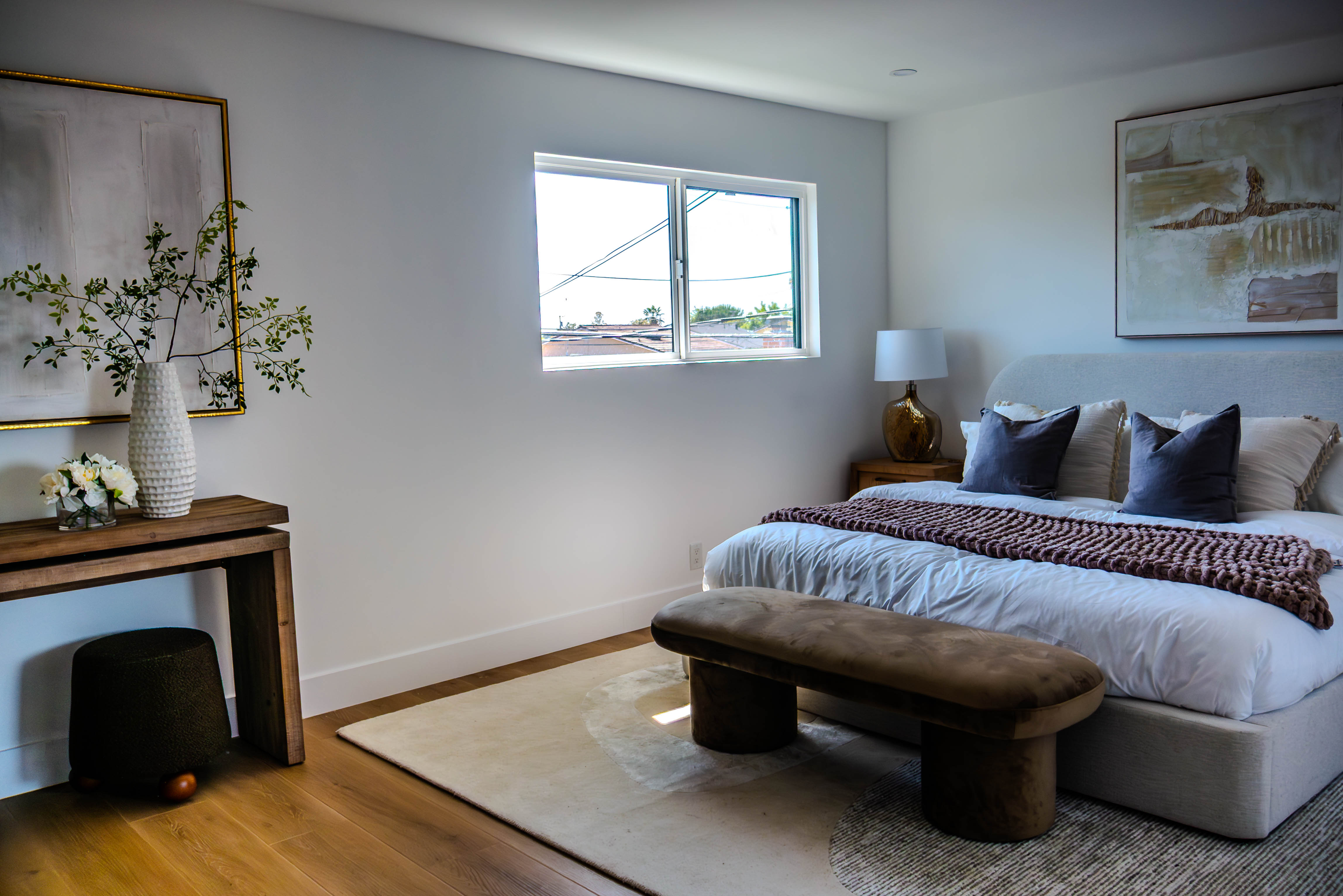 Sophisticated master bedroom with white platform bed, navy blue accent pillows, chunky knit throw, and modern bench