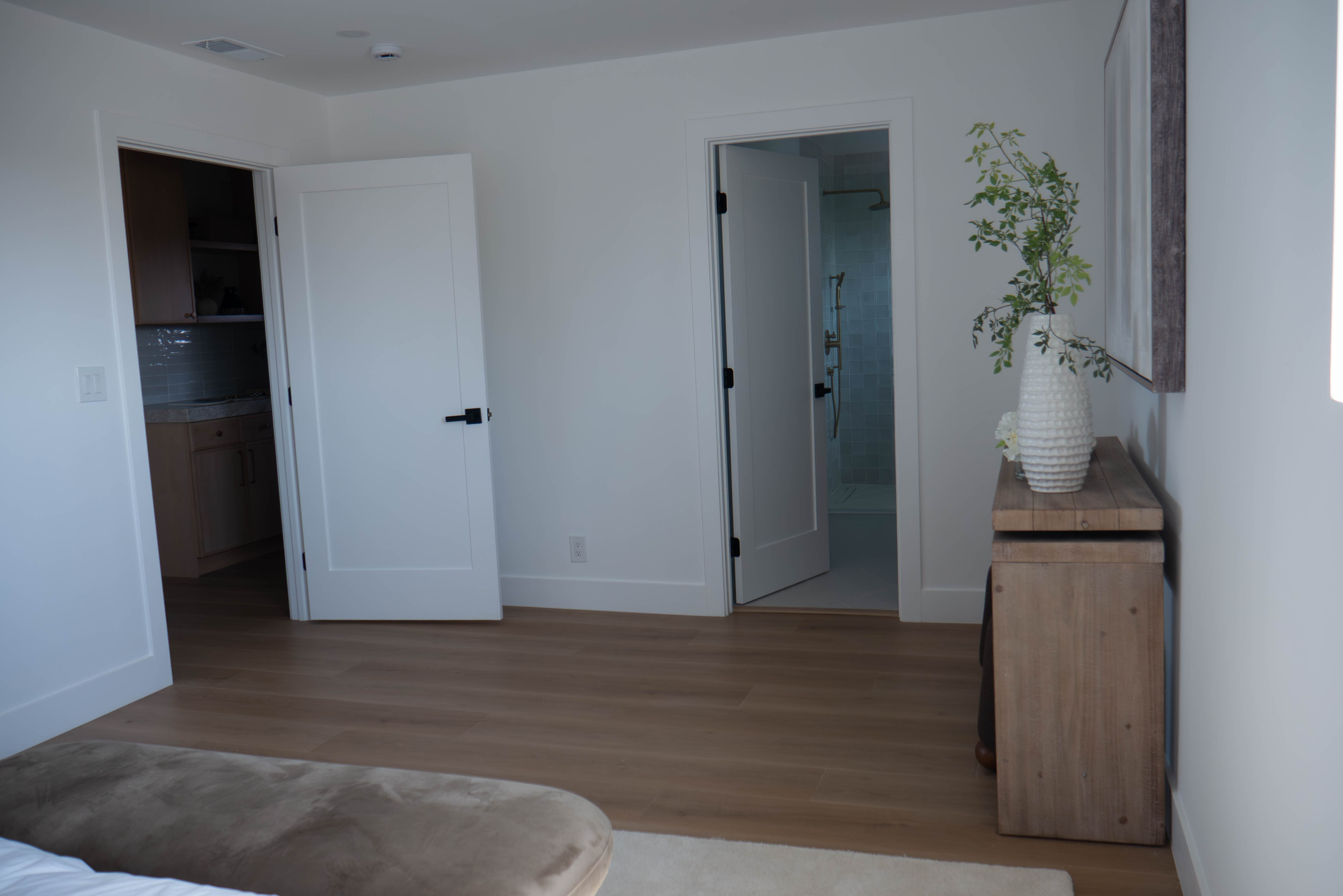 Master bedroom with hardwood flooring and view into en-suite bathroom with sage green tile