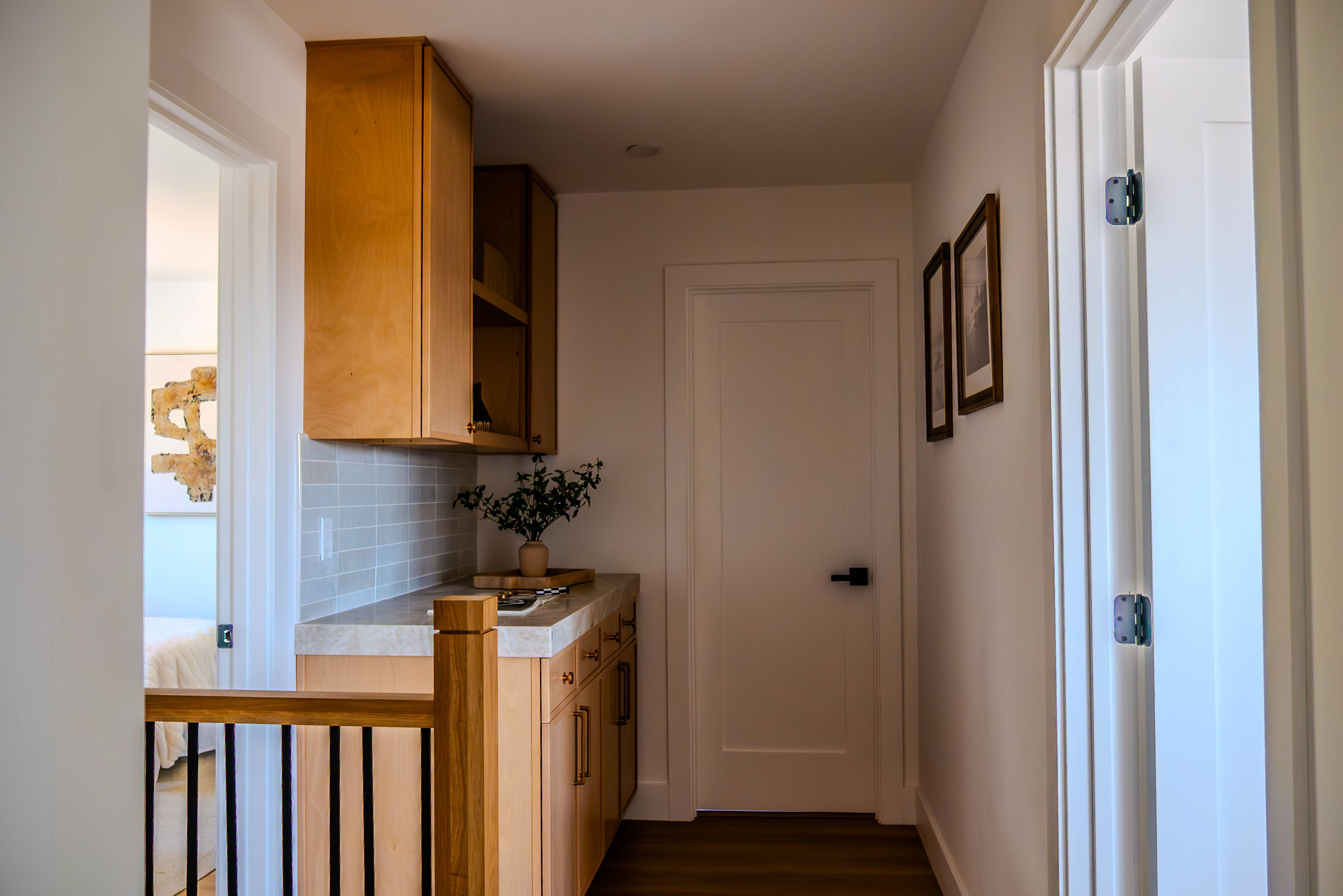 Upper level kitchen area with natural wood cabinetry, white countertops, light blue subway tile backsplash, and modern black hardware