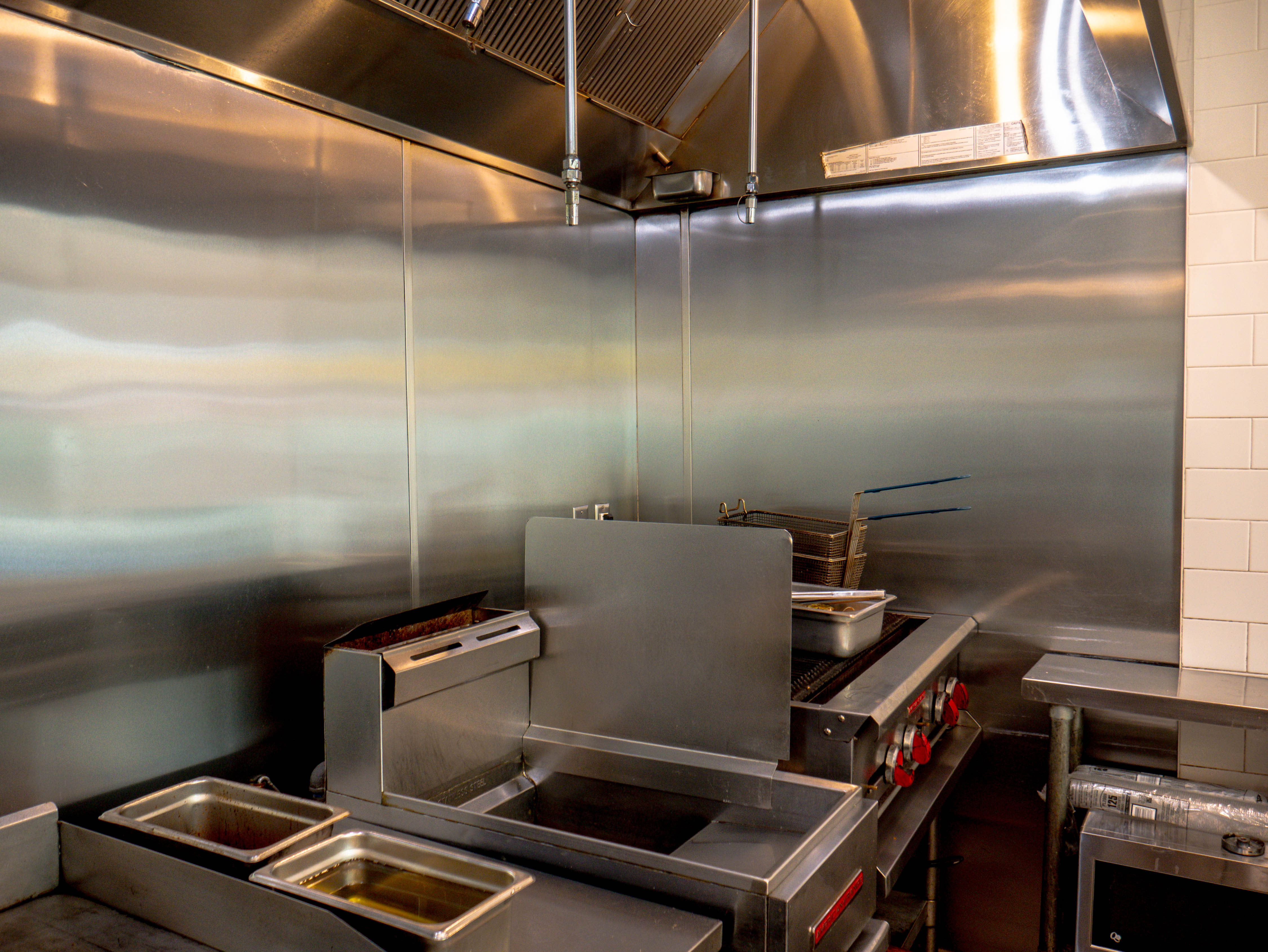 Professional commercial kitchen with stainless steel surfaces, fryer, ventilation hood, and organized cooking equipment