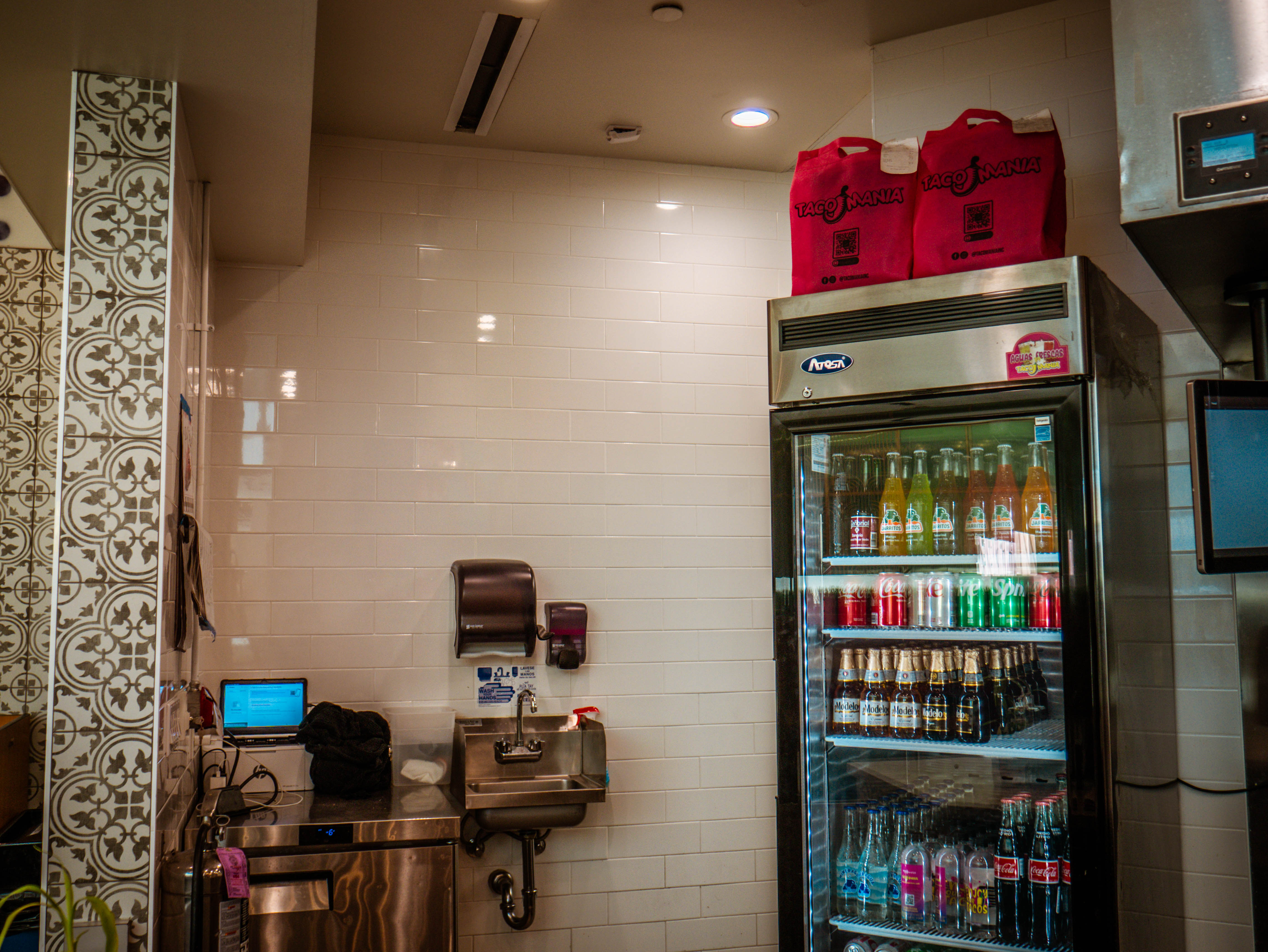 Service area with beverage cooler, hand washing station, TacoMania branded bags, and commercial equipment installations
