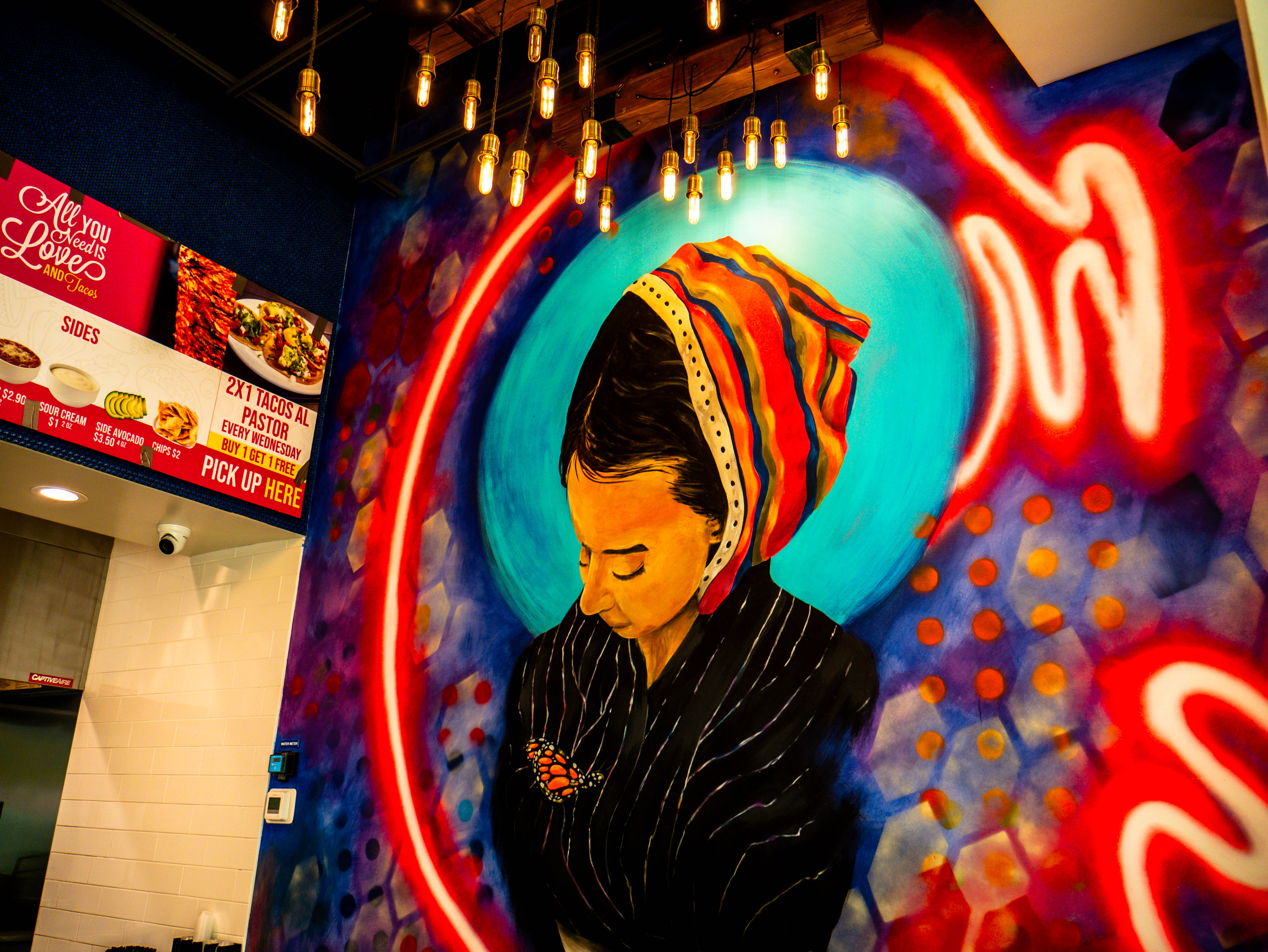 Artistic mural of woman with traditional headwrap featuring neon-style lighting effects and service counter view
